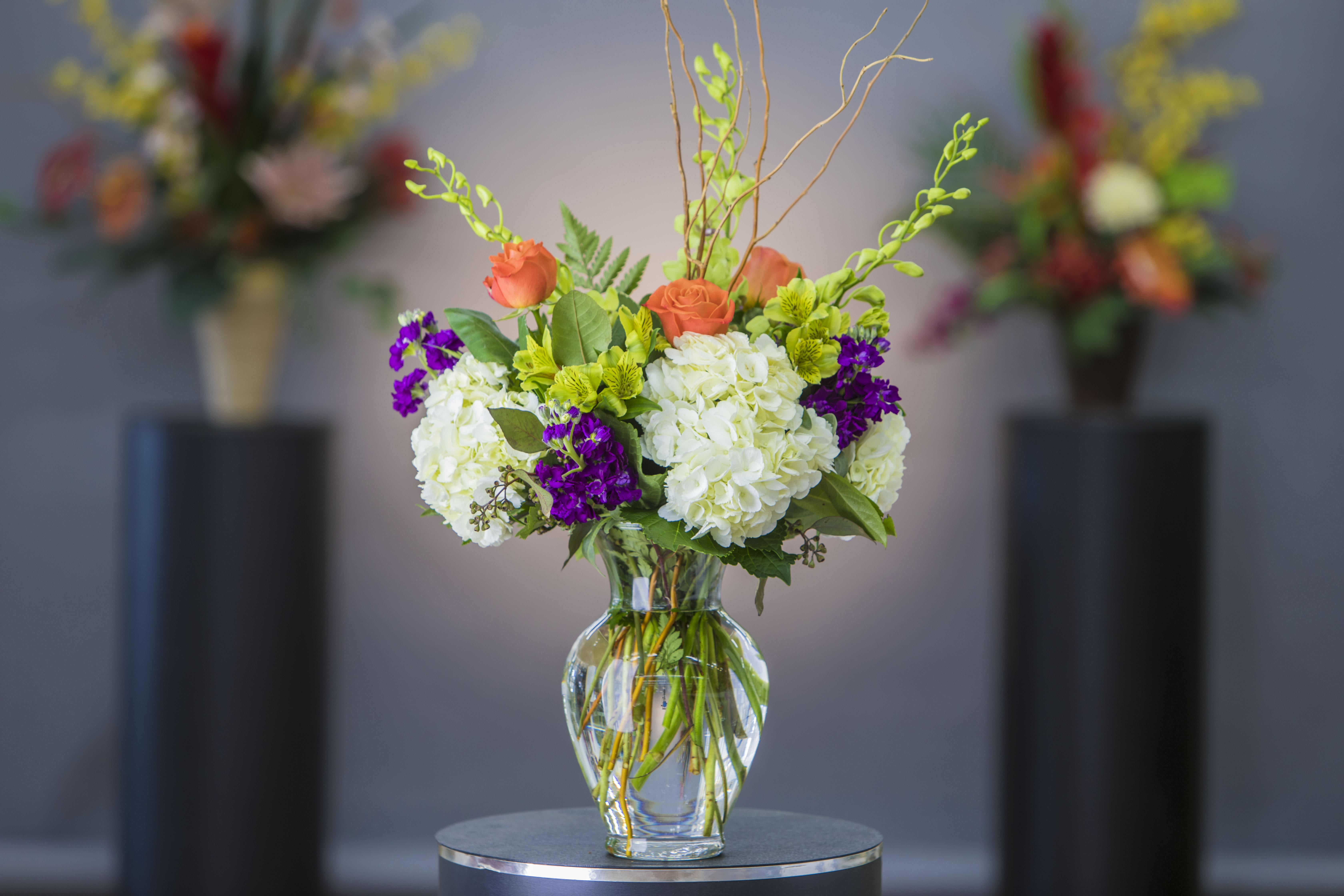 Mixed bouquet of white hydrangeas, orange roses, and purple flowers in a glass vase