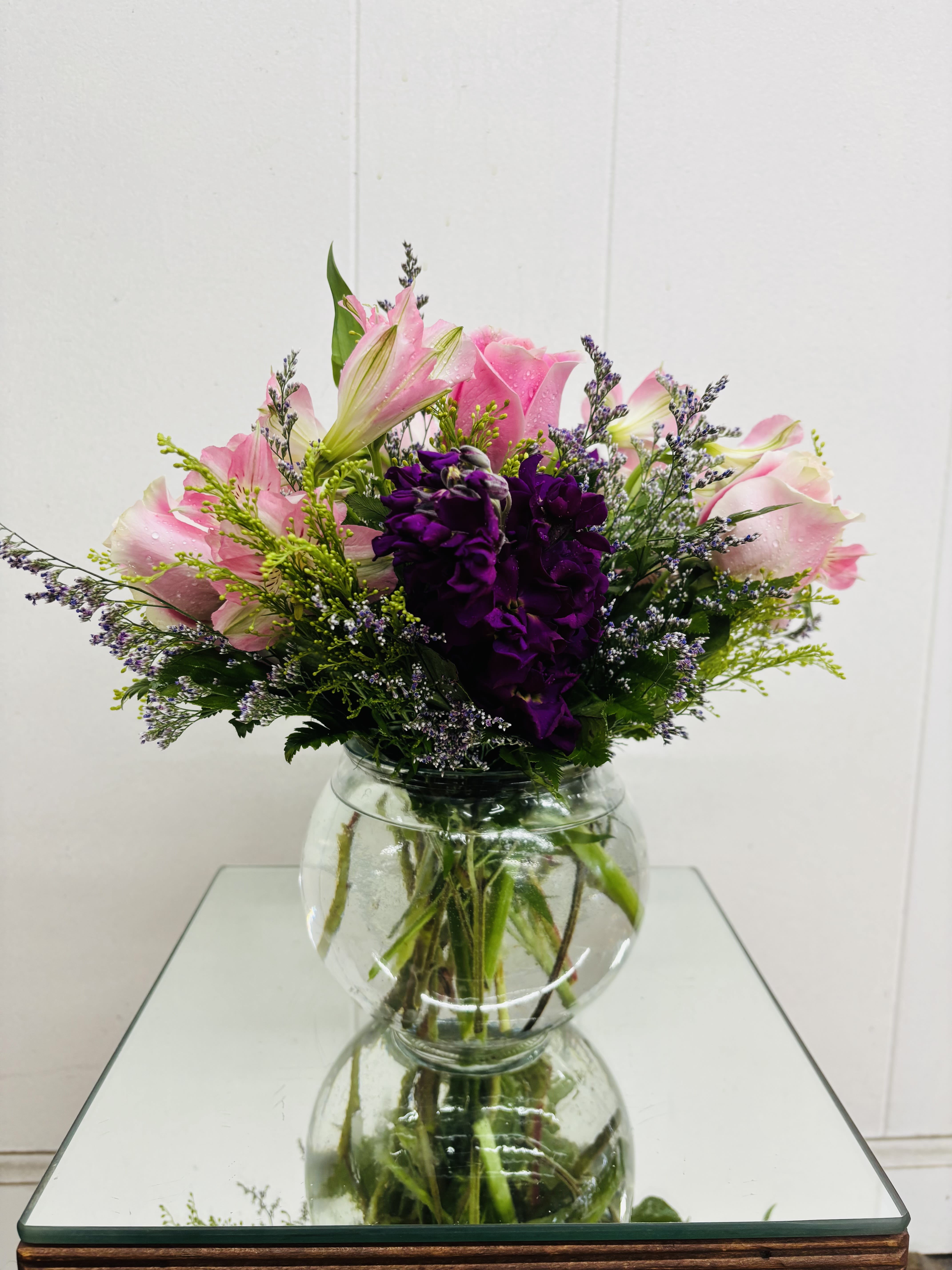 Pink lilies and purple flowers arranged in a clear glass vase