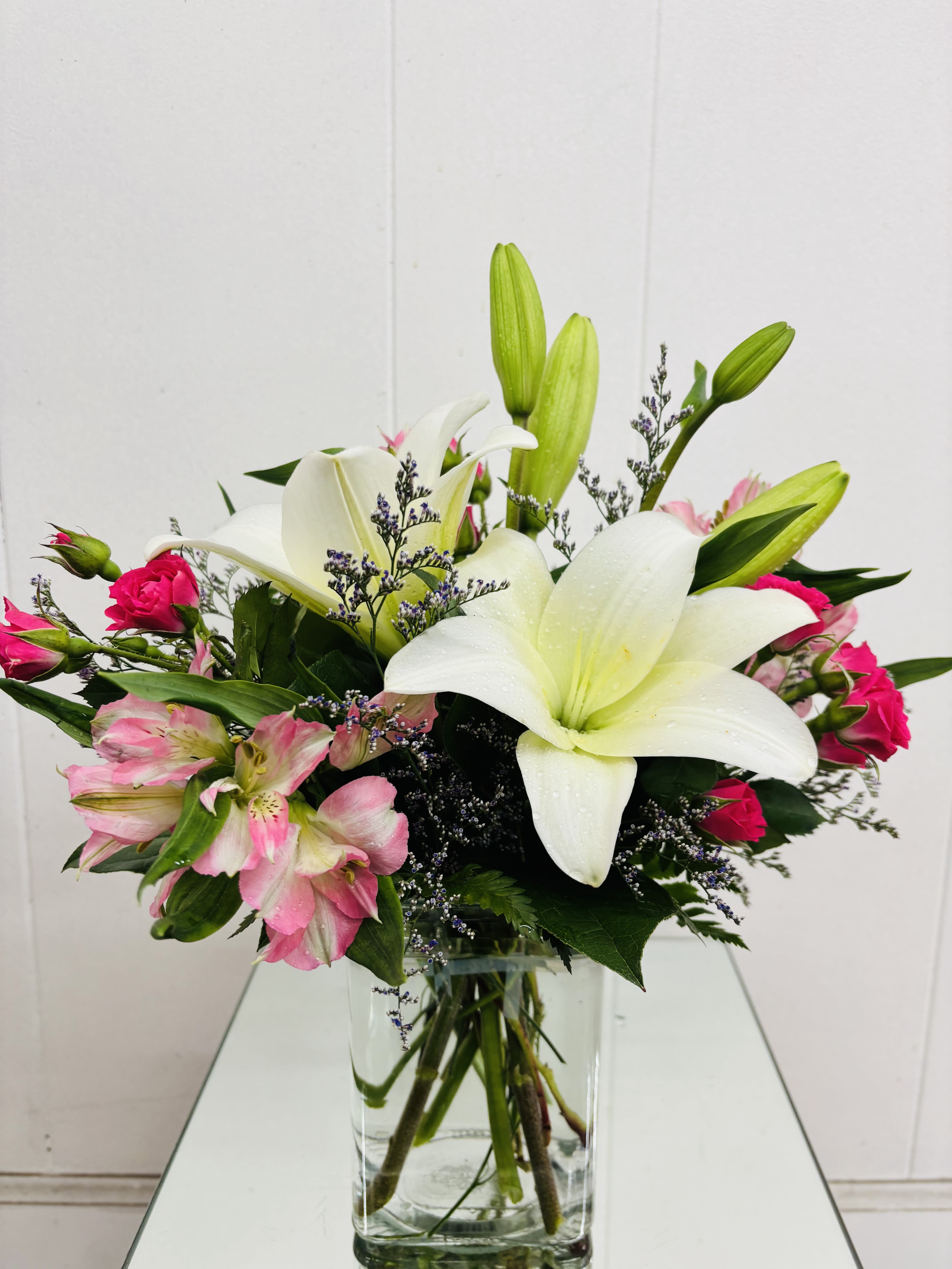White lilies and pink flowers arranged in a clear glass vase