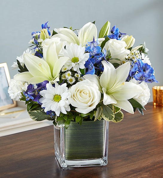 White lilies, roses, and blue flowers in a square glass vase