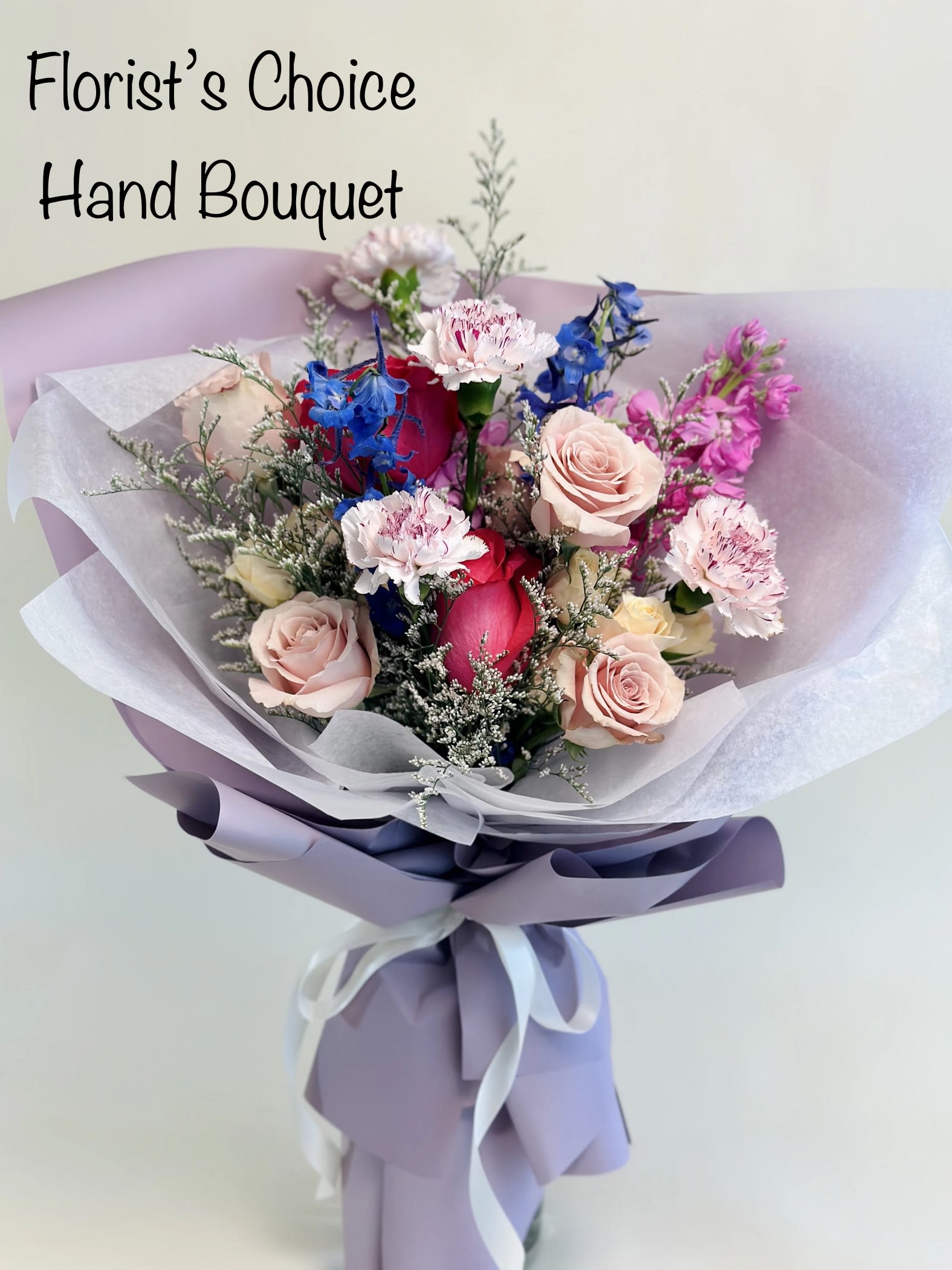 Hand bouquet of pink roses, carnations, and blue flowers wrapped in lavender paper