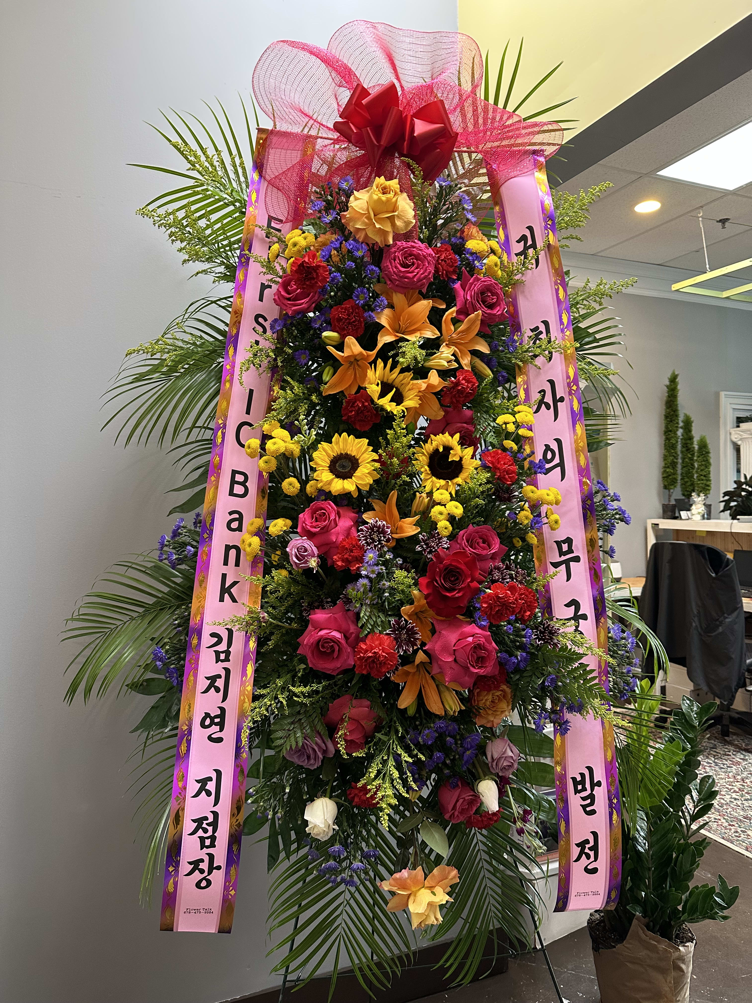 Tall standing floral wreath with pink ribbons and mixed blooms