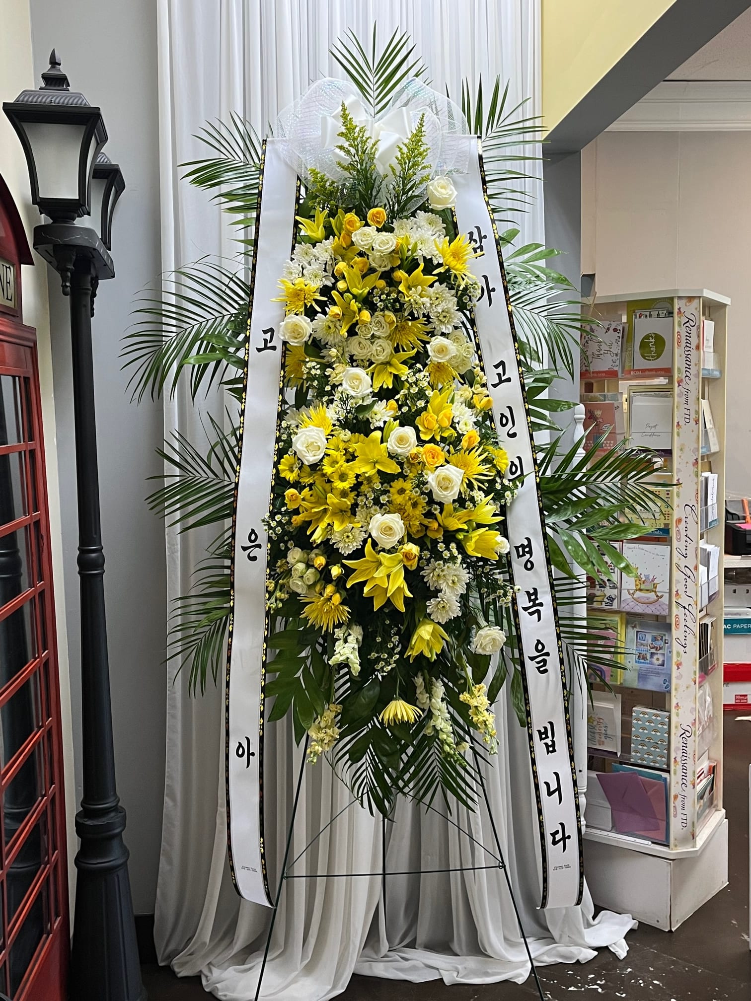 Tall standing floral wreath with yellow and white flowers on a ribboned easel