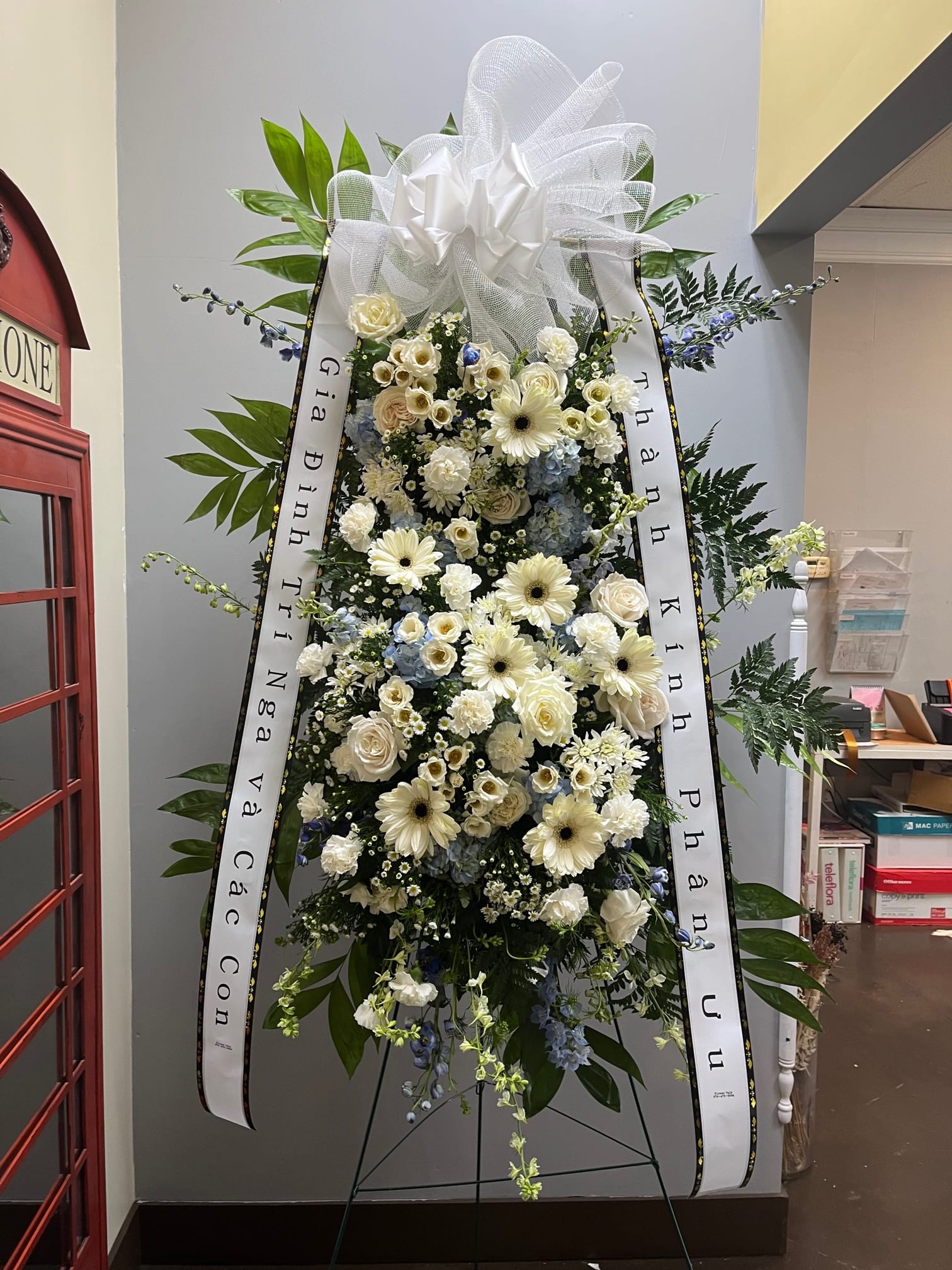 Standing funeral spray of white and pale blue flowers with ribbons
