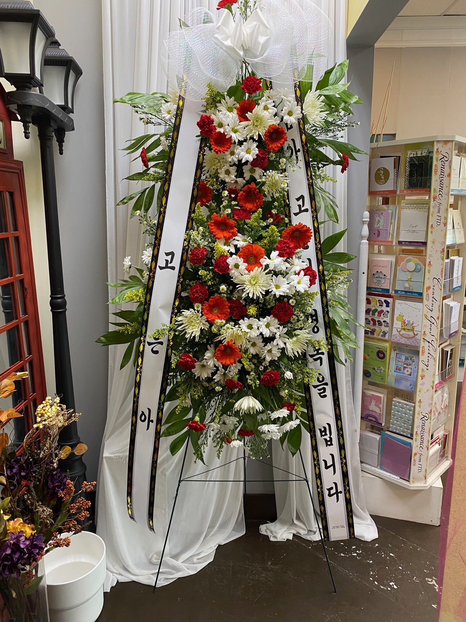 Tall standing floral spray with white ribbons and red, white, and orange flowers