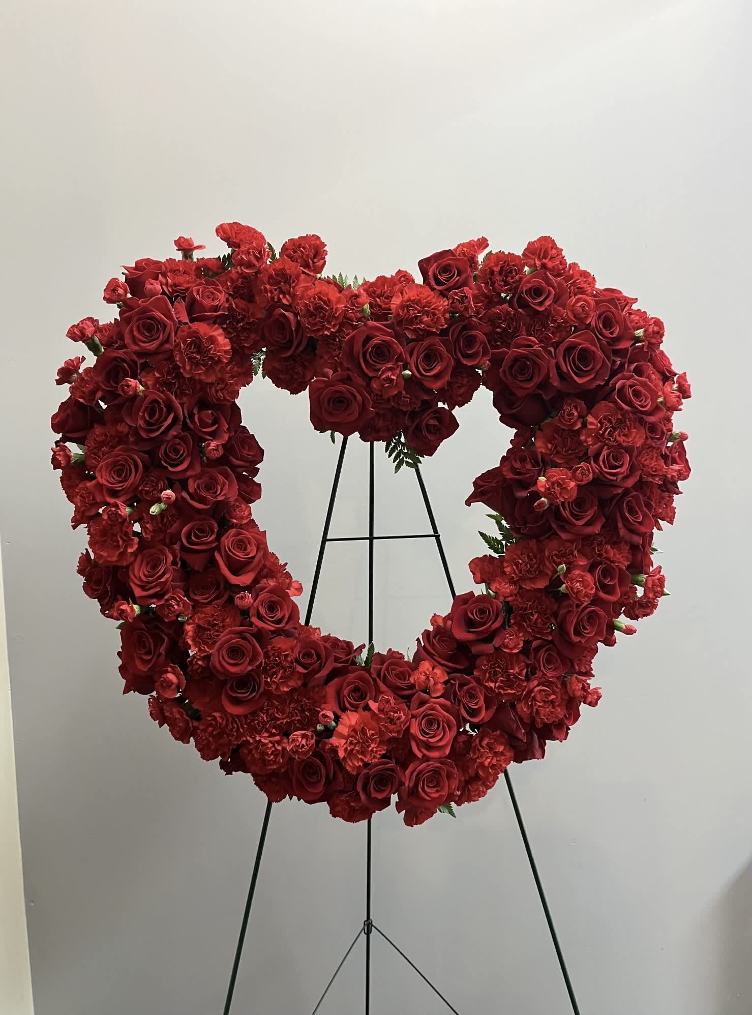 Heart-shaped red rose and carnation floral wreath on a stand