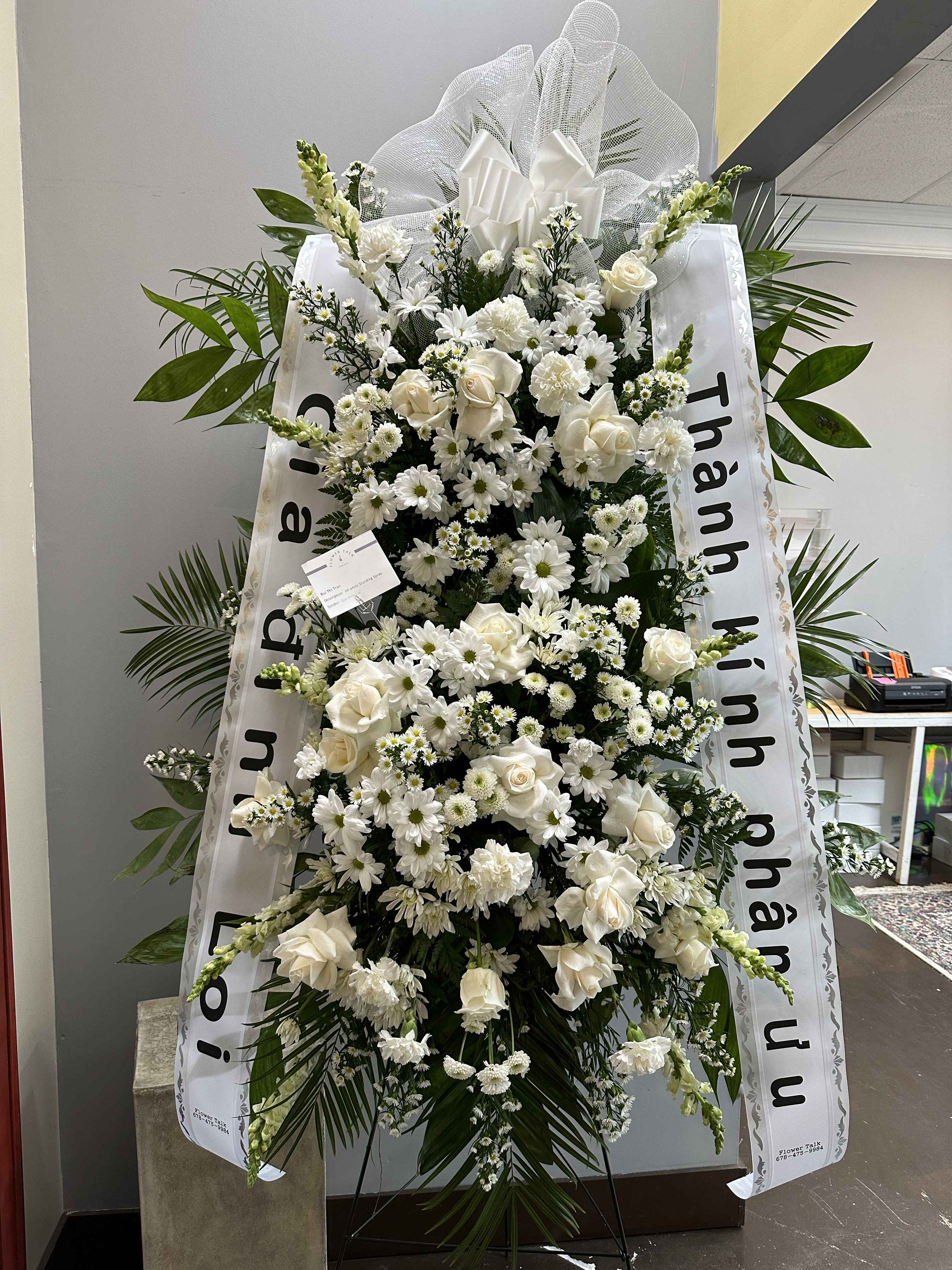 Large white funeral standing spray with roses and daisies on a ribboned easel