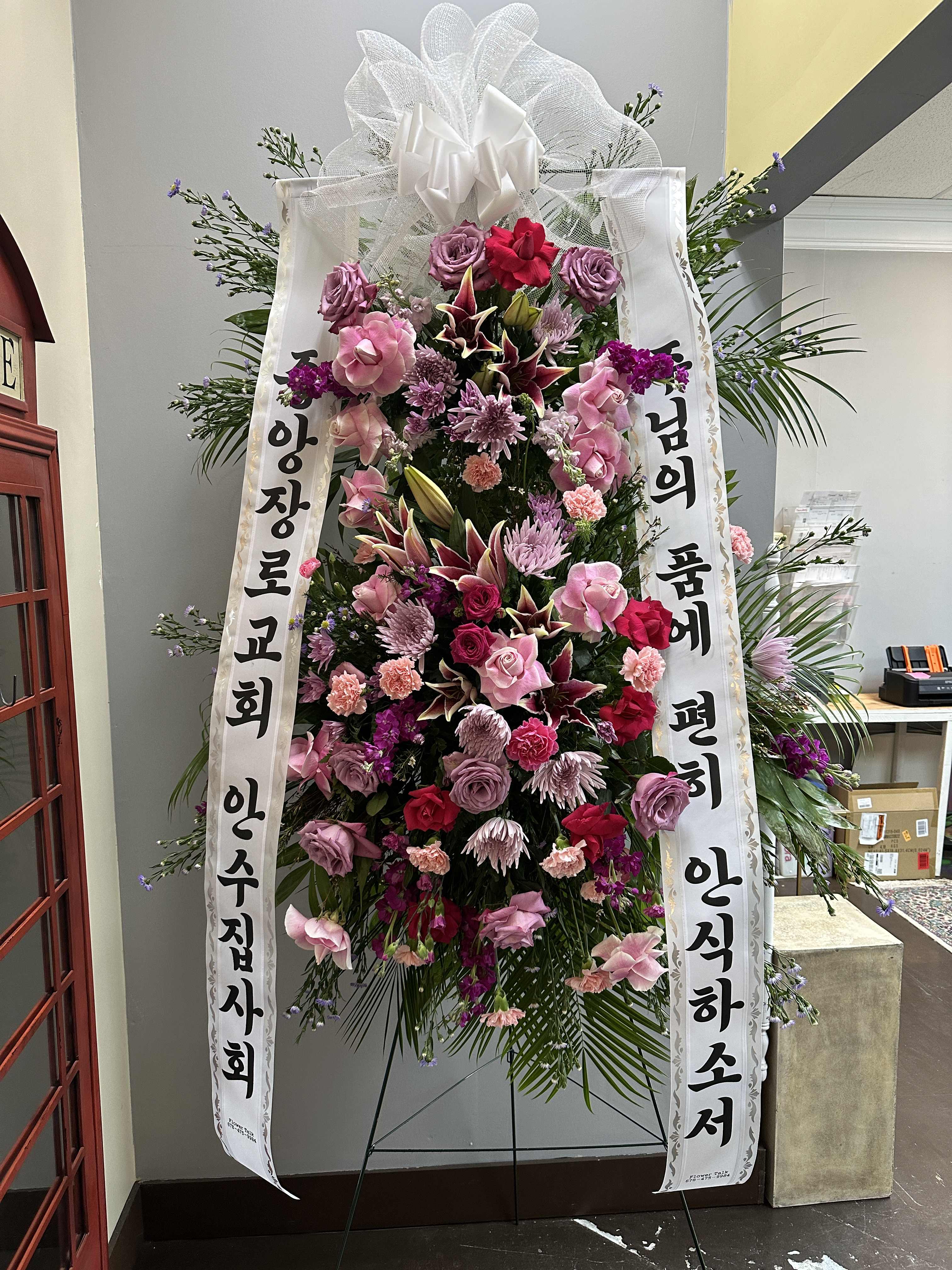 Tall standing floral wreath with pink and purple flowers and white ribbons