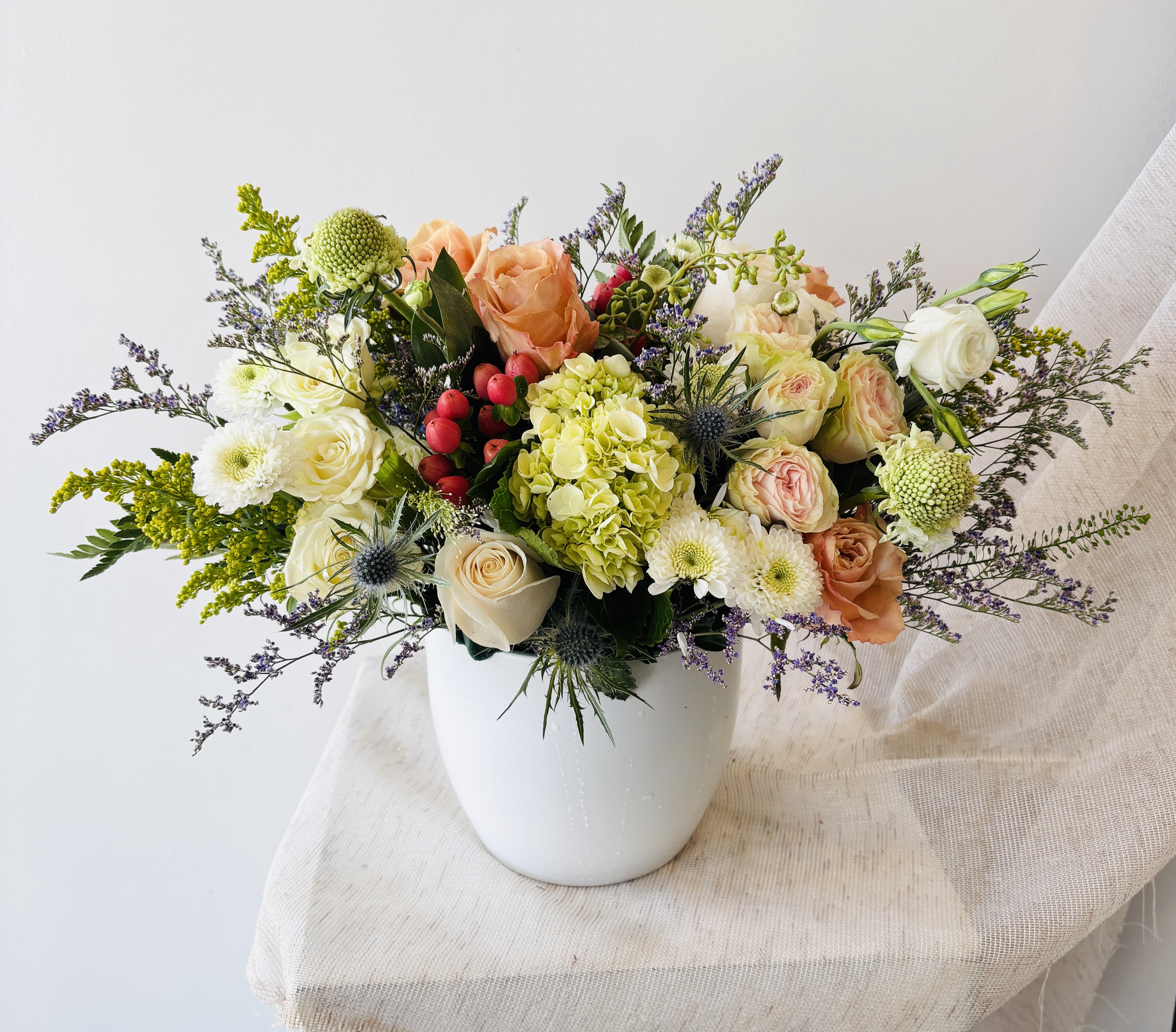 Mixed bouquet of peach, white, and green flowers in a white vase