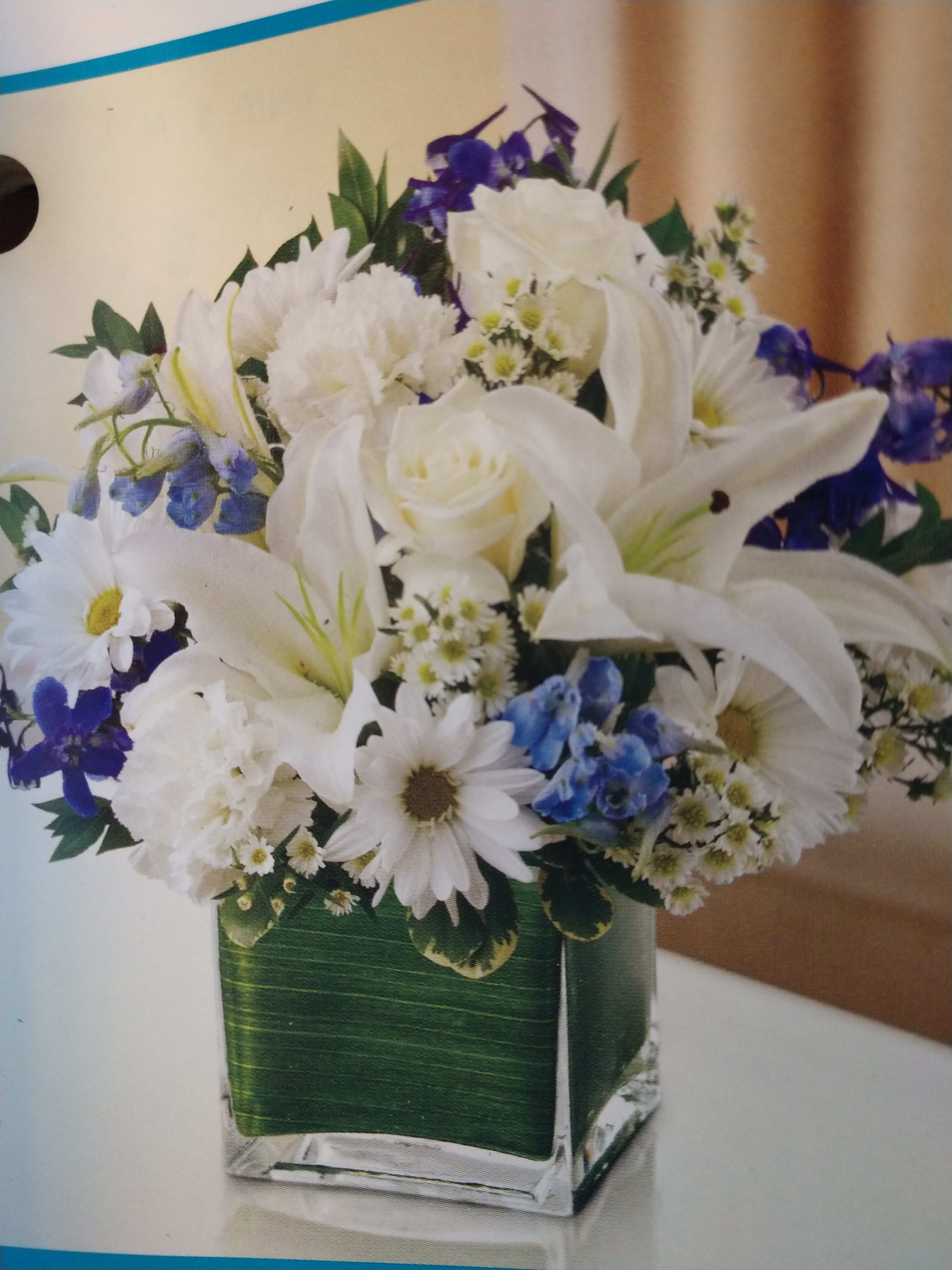 White lilies and daisies with blue flowers in a square glass vase