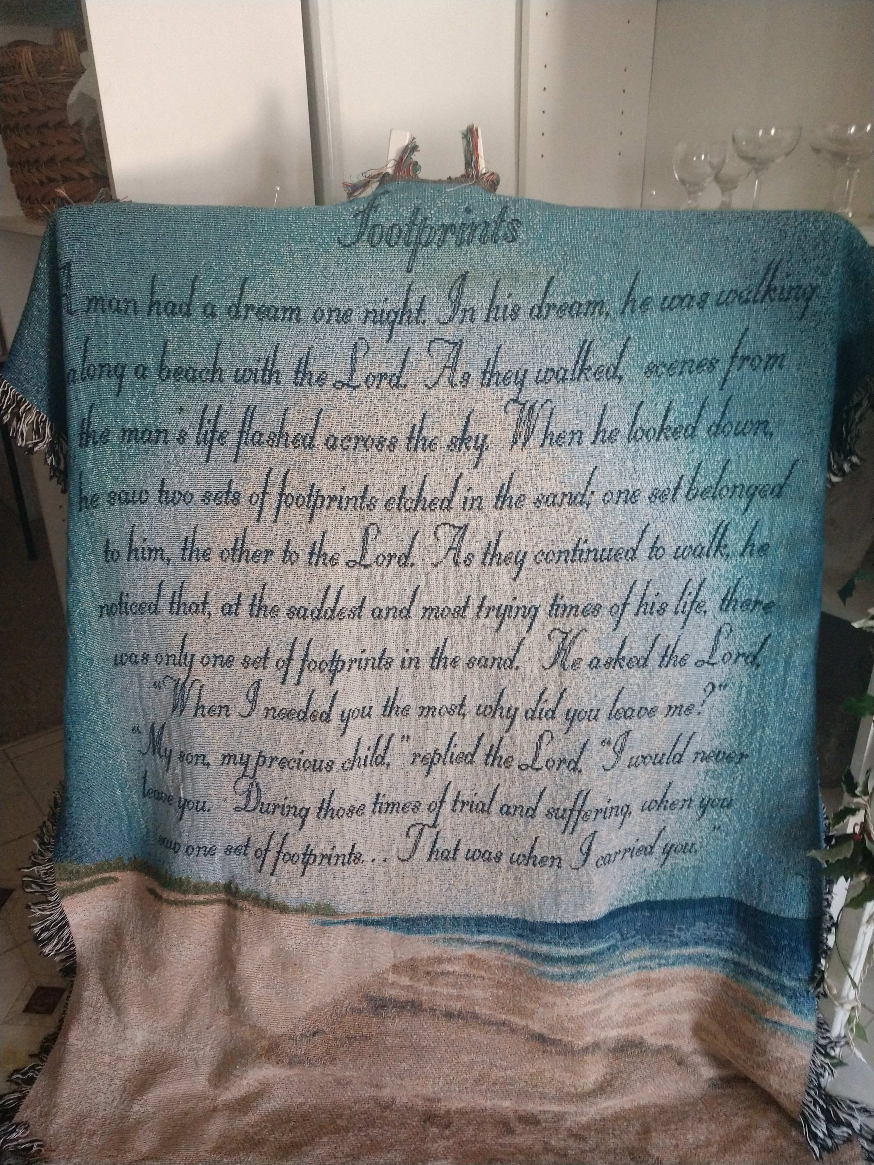 A woven blanket with a beach scene and printed text hangs over a chair