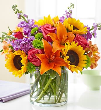 Floral Embrace -  Send our truly original arrangement to let your special someone embrace their inner interior decorator. Crafted by our expert florists from the freshest roses, lilies, stock, sunflowers and alstroemeria in a classic cylinder vase, its compact beauty is perfect for impressing friends and family or for simply dressing up any room in the home. Vibrant arrangement of roses, lilies, sunflowers, stock, alstroemeria, poms and monte casino, gathered with fresh salal Artistically designed in an elegant glass cylinder vase; measures 6"H Large arrangement measures approximately 13"H x 13"L Medium arrangement measures approximately 12"H x 12"L Small arrangement measures approximately 11"H x 11"L Our florists hand-design each arrangement, so colors, varieties, and basket may vary due to local availability Lilies may arrive in bud form and will open to full beauty over the next 2-3 days