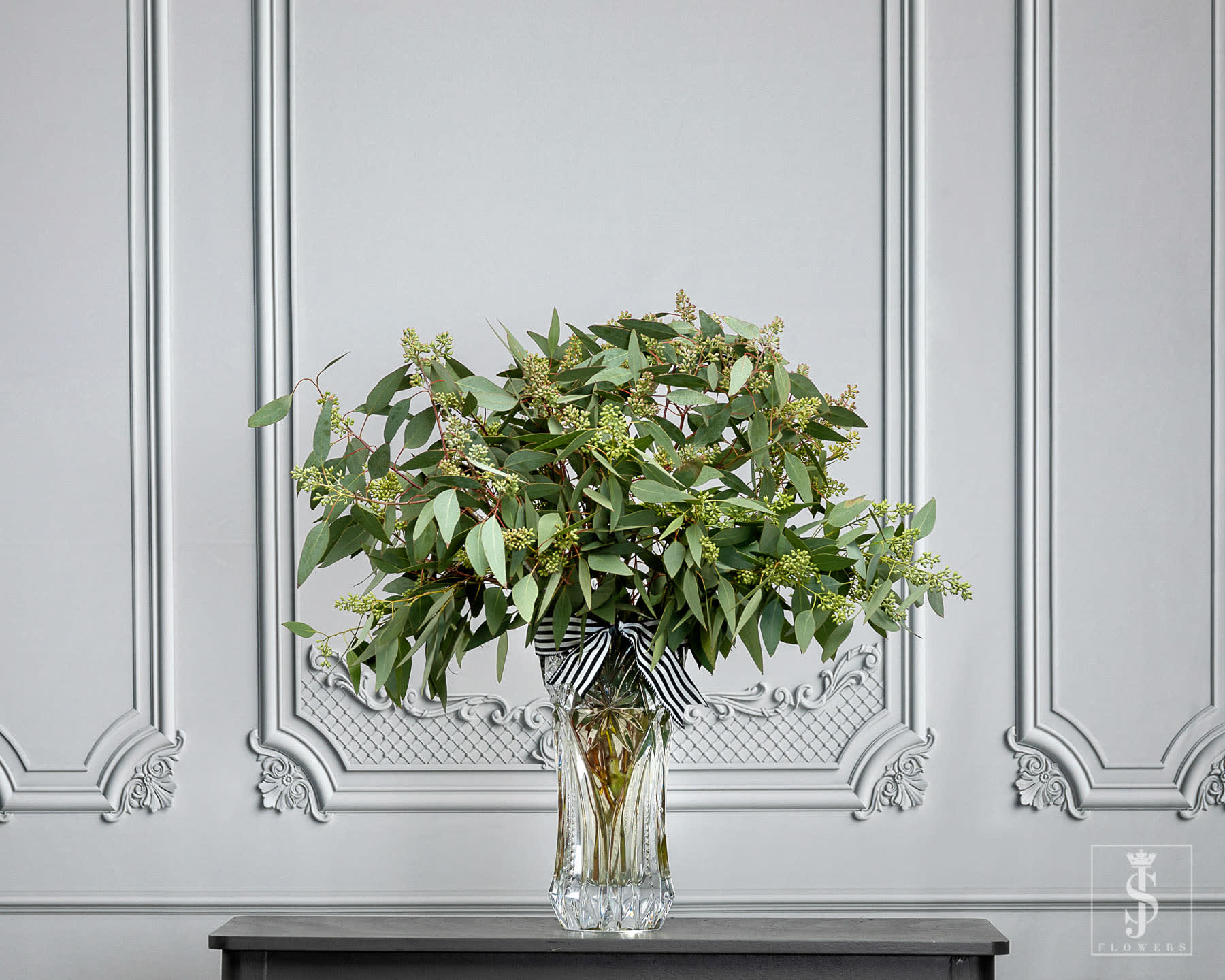 Green foliage arrangement in a clear glass vase with a striped ribbon