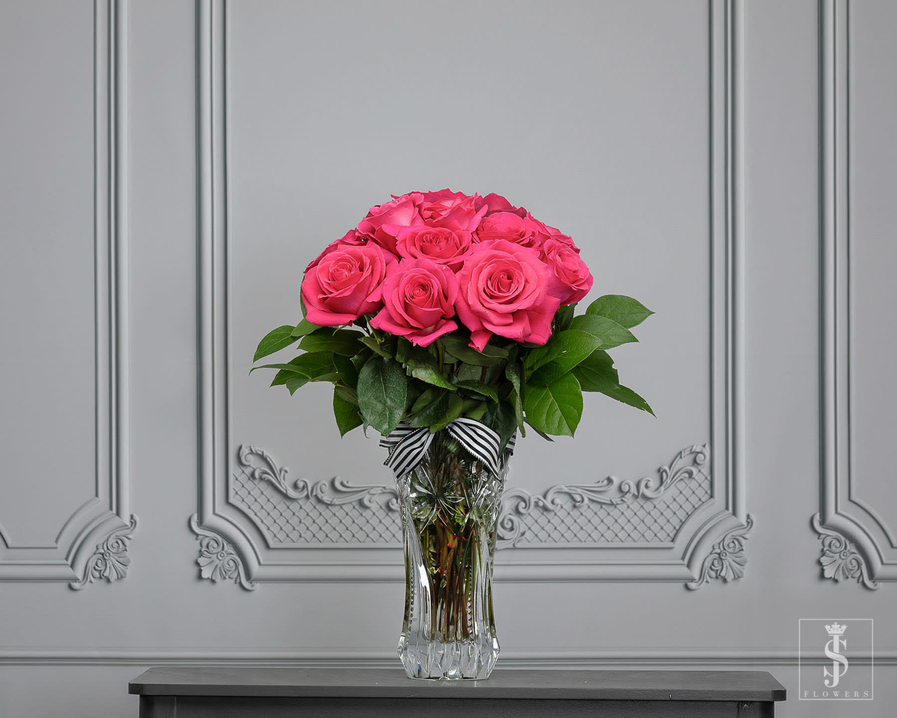 Pink roses arranged in a clear glass vase with a striped ribbon