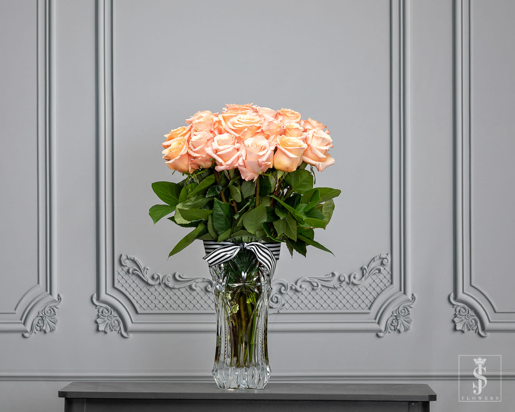 Peach roses arranged in a clear glass vase with a striped ribbon.