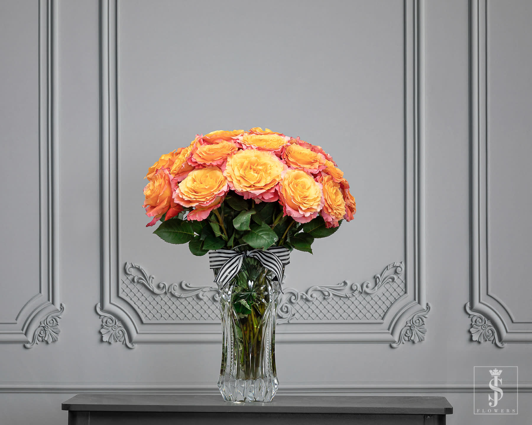 Orange and pink roses arranged in a clear glass vase with a striped ribbon