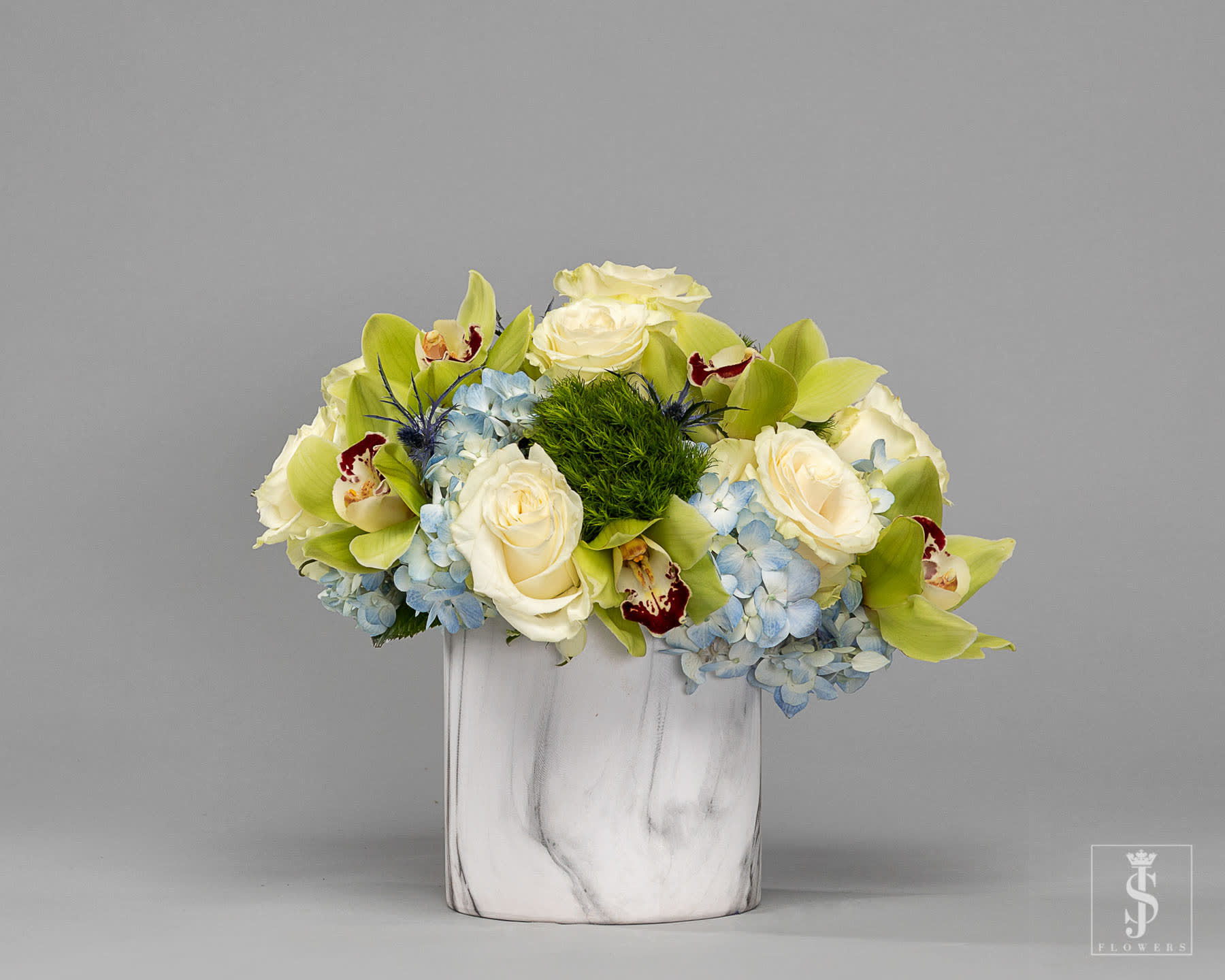 White roses and blue hydrangeas in a white vase with green orchids
