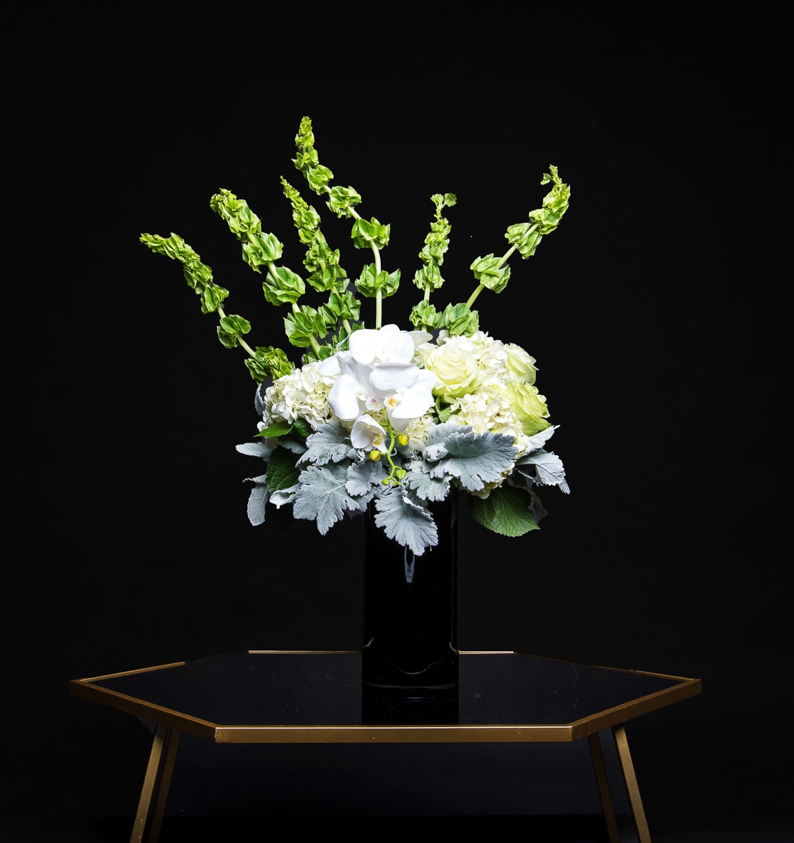 White orchids and pale hydrangeas in a black vase with tall green spikes
