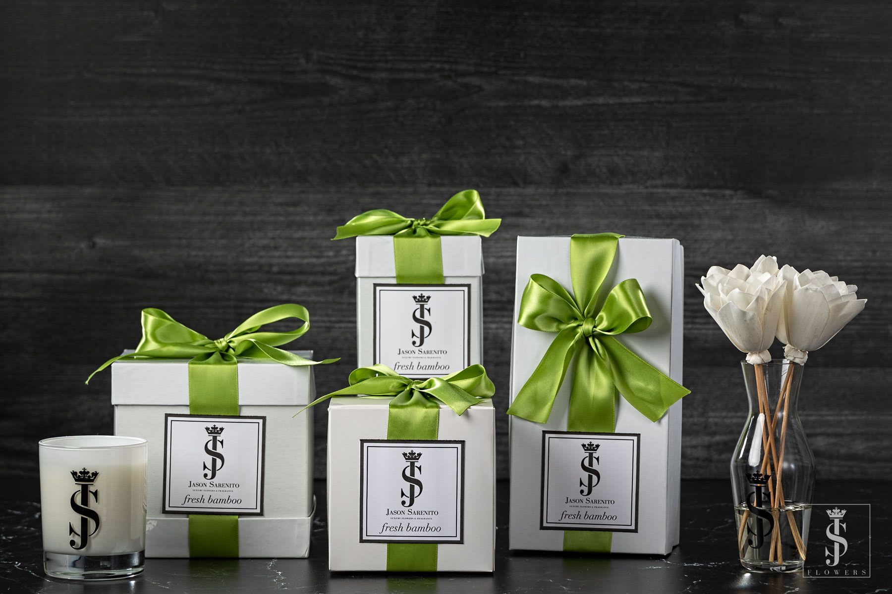 Gift boxes with green ribbons, a candle, and white flowers in a vase