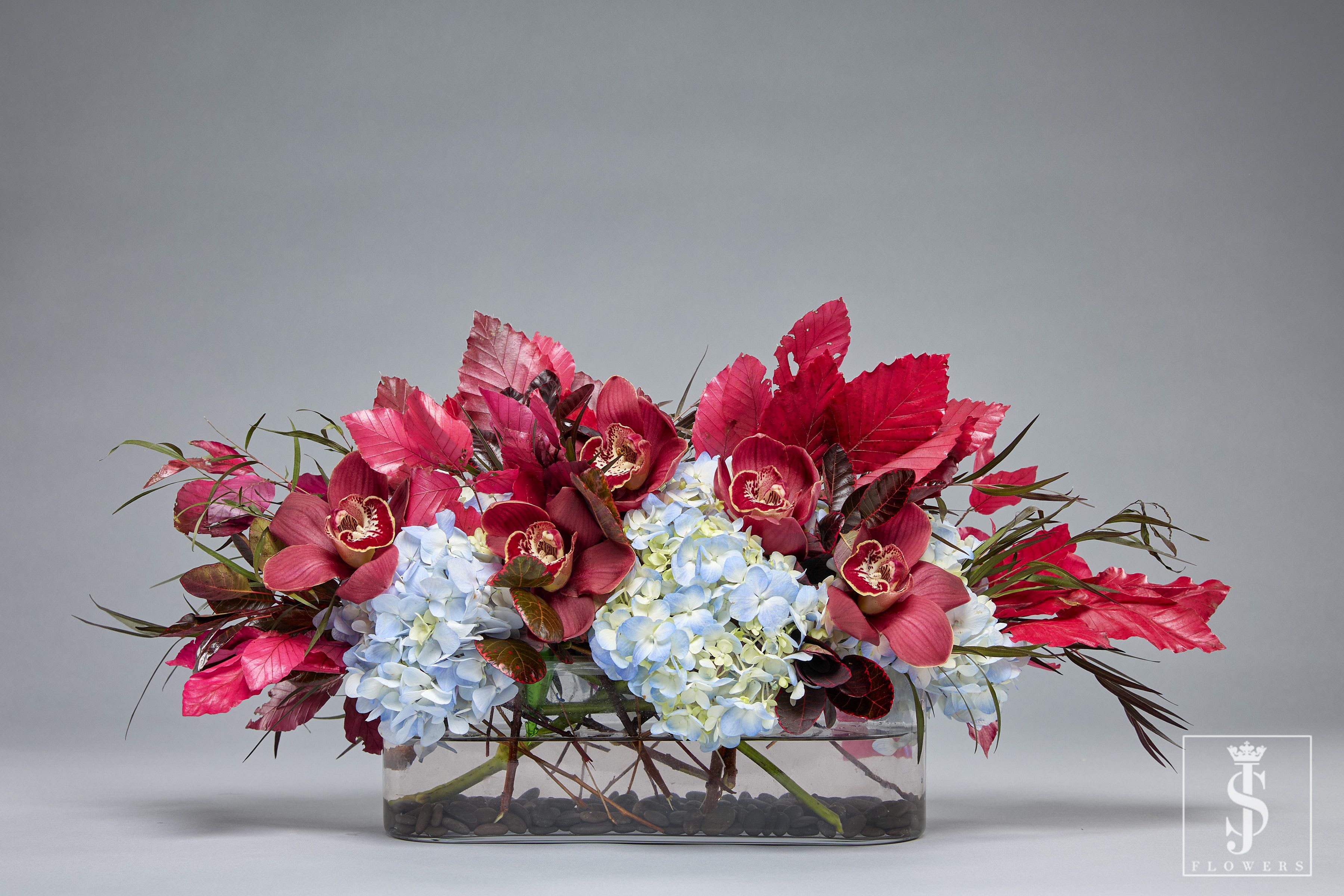 Low floral arrangement with blue hydrangeas and burgundy orchids in a glass vase