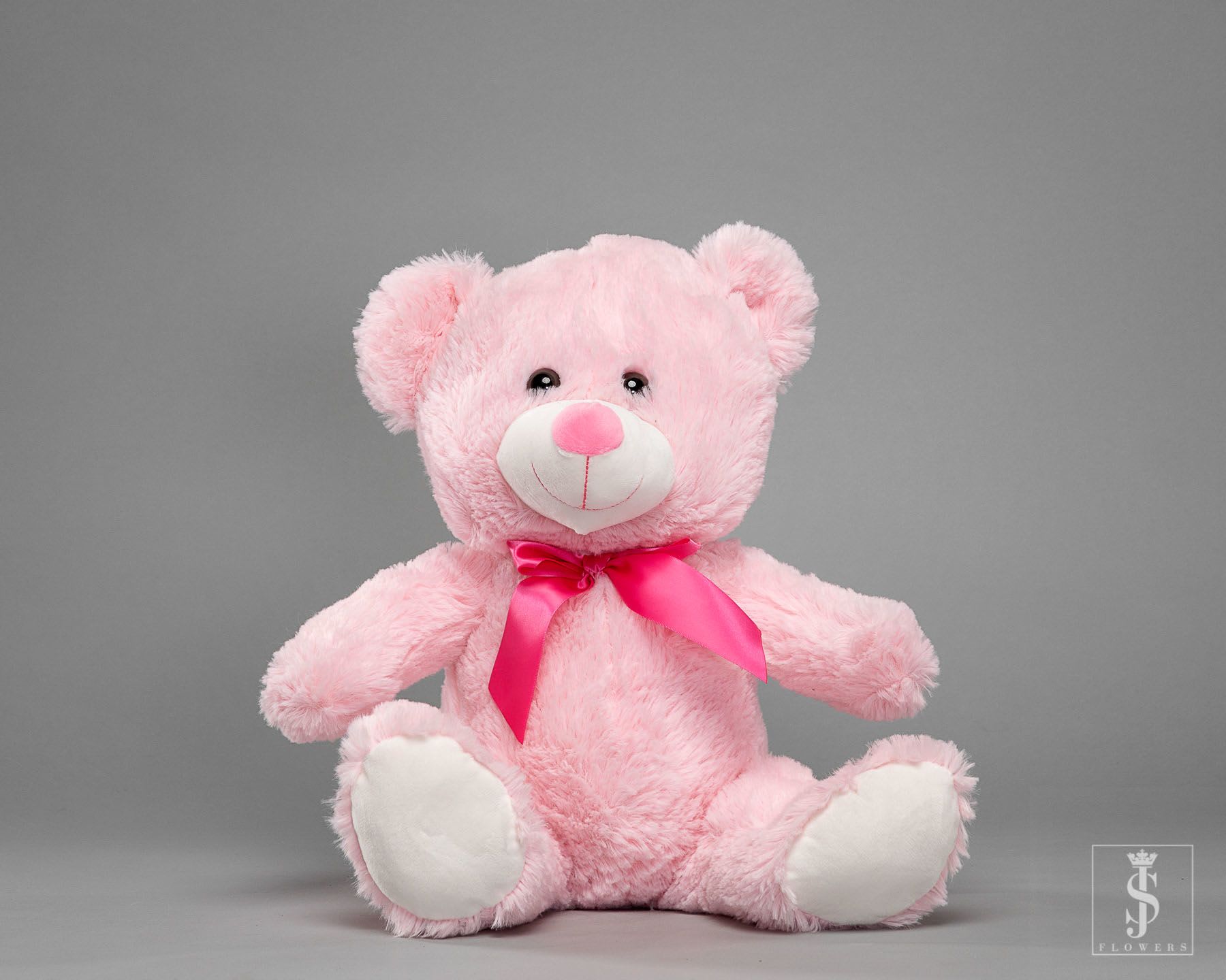 Pink teddy bear with a satin ribbon sitting on a gray background