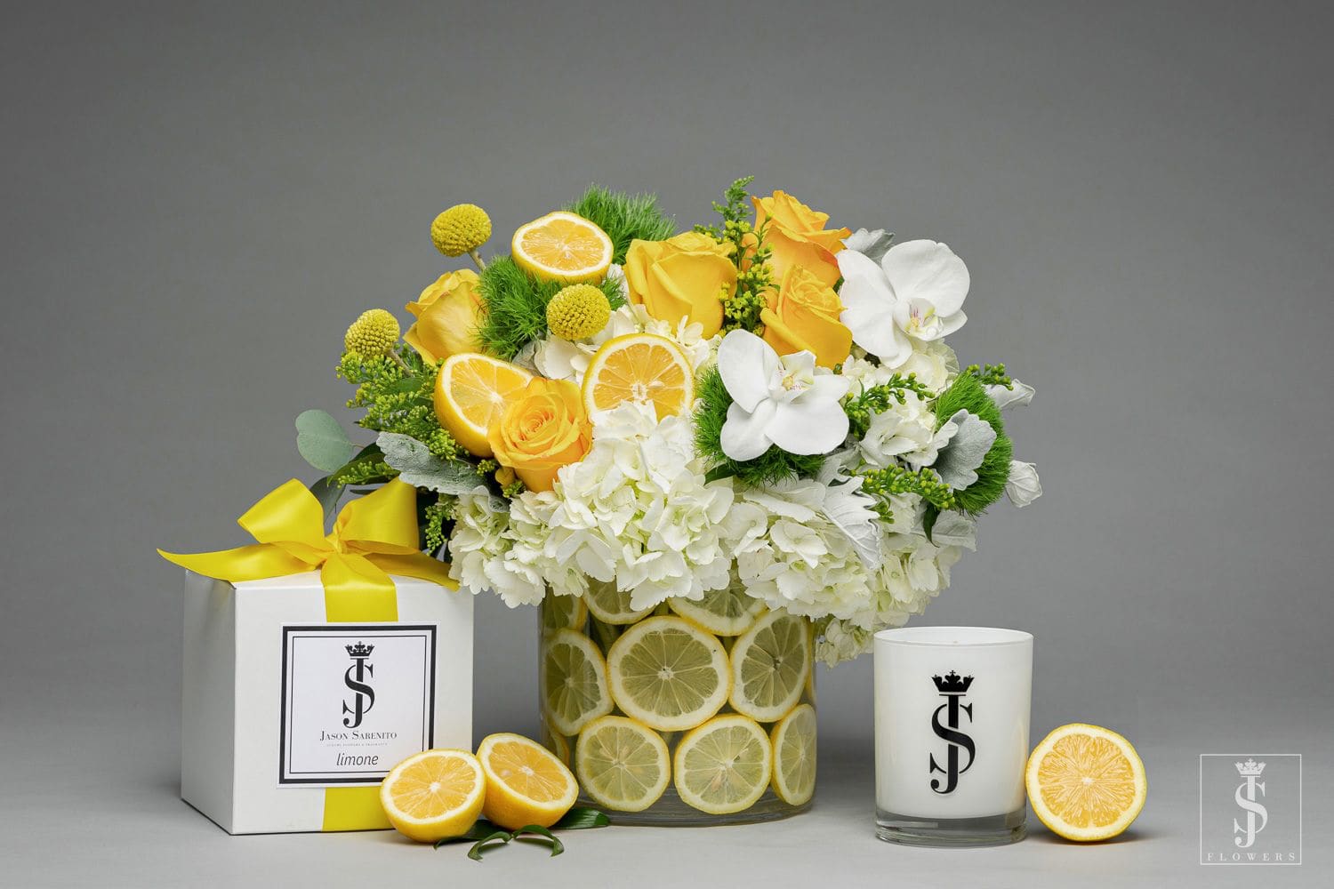 Yellow and white floral arrangement in a lemon-decorated vase with a gift box and candle