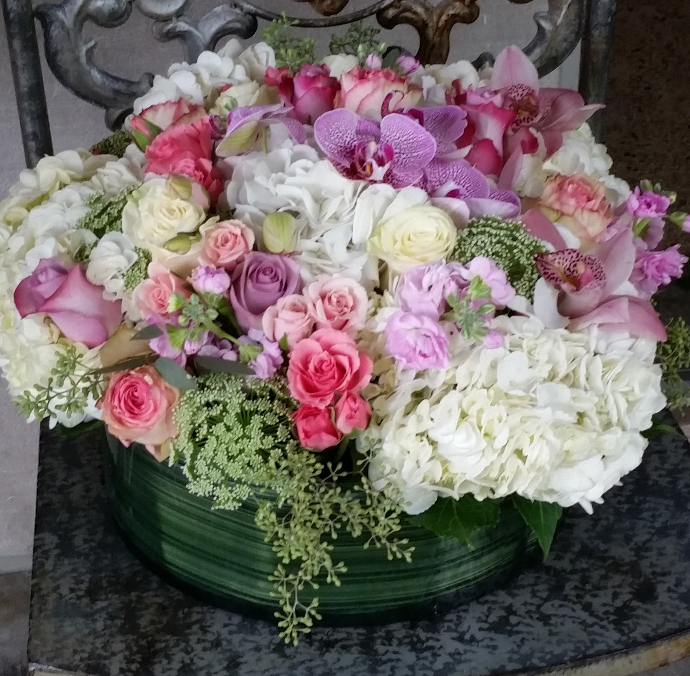 Round arrangement of pink and white roses, hydrangeas, and orchids in a green container