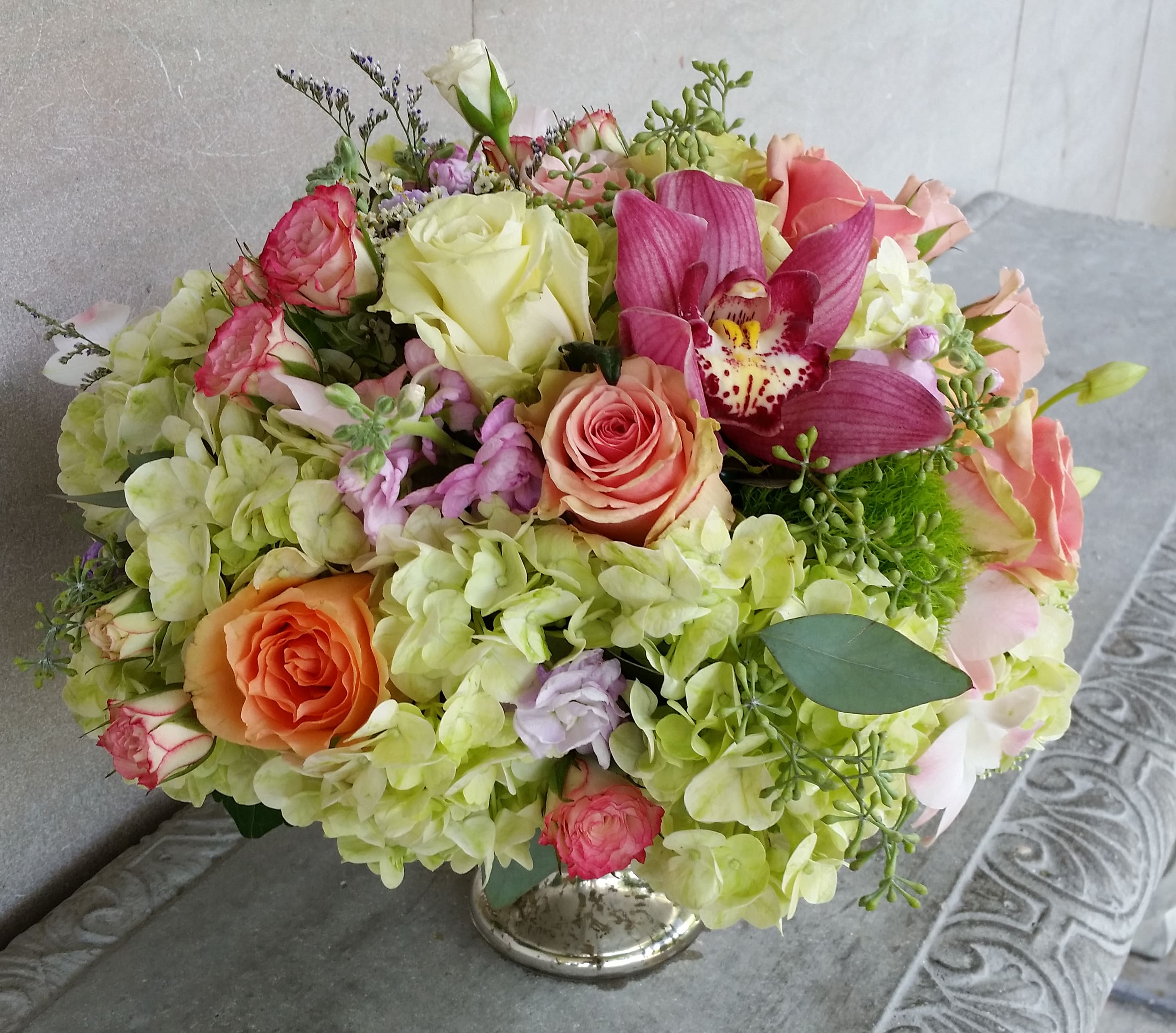 Bouquet of pink and peach roses with green hydrangeas and a magenta orchid