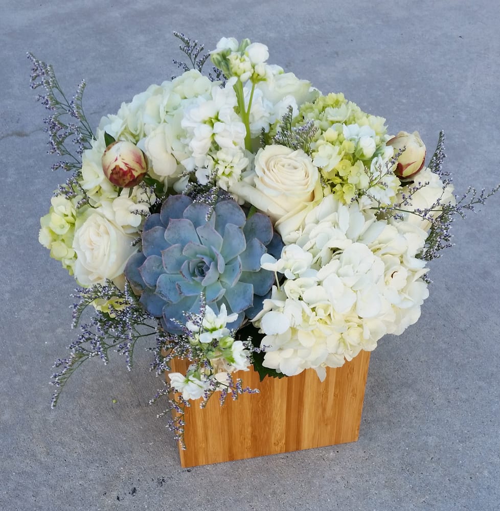 White floral arrangement with a blue succulent in a wooden box