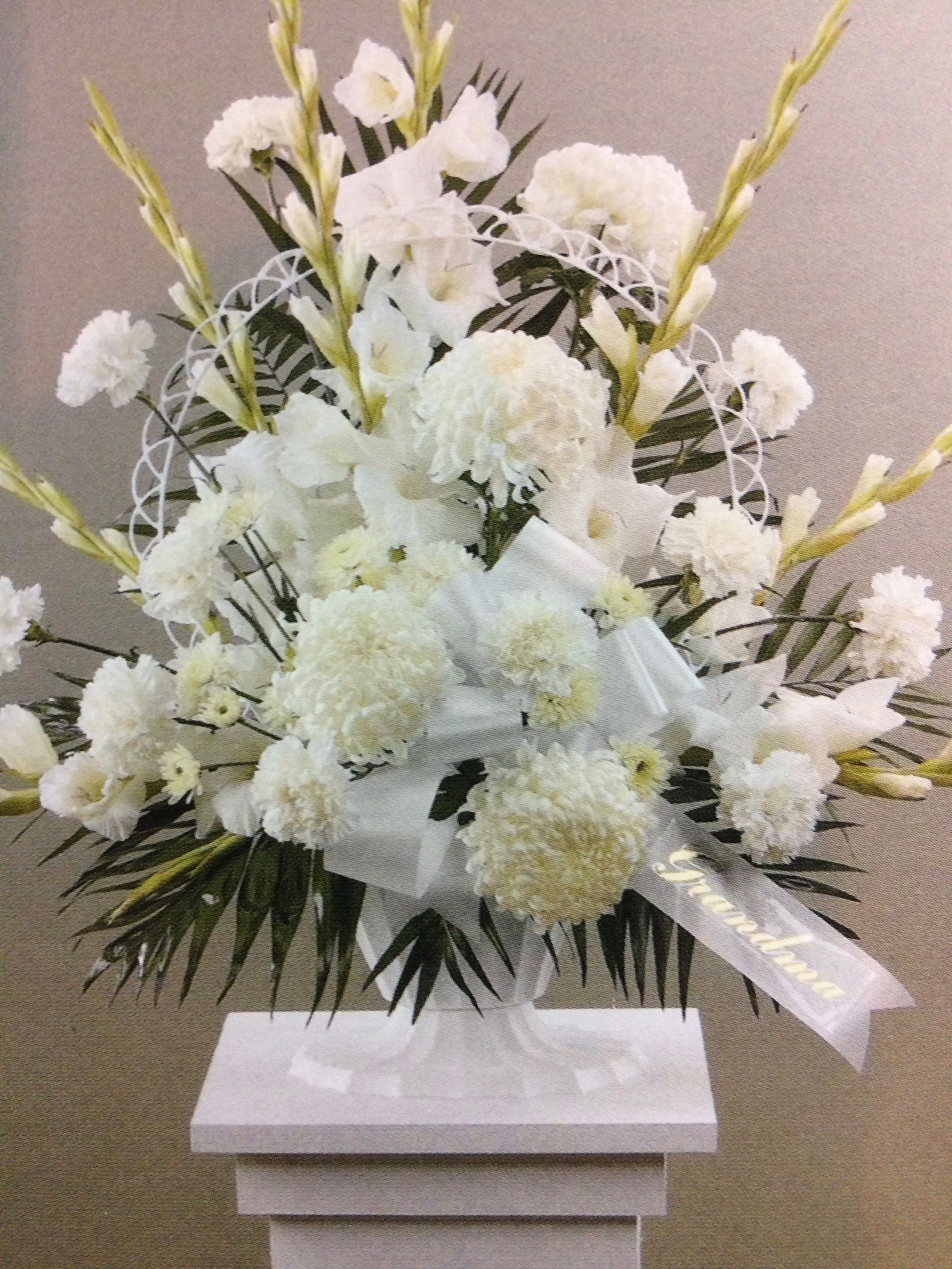White floral standing arrangement with ribbon on a pedestal
