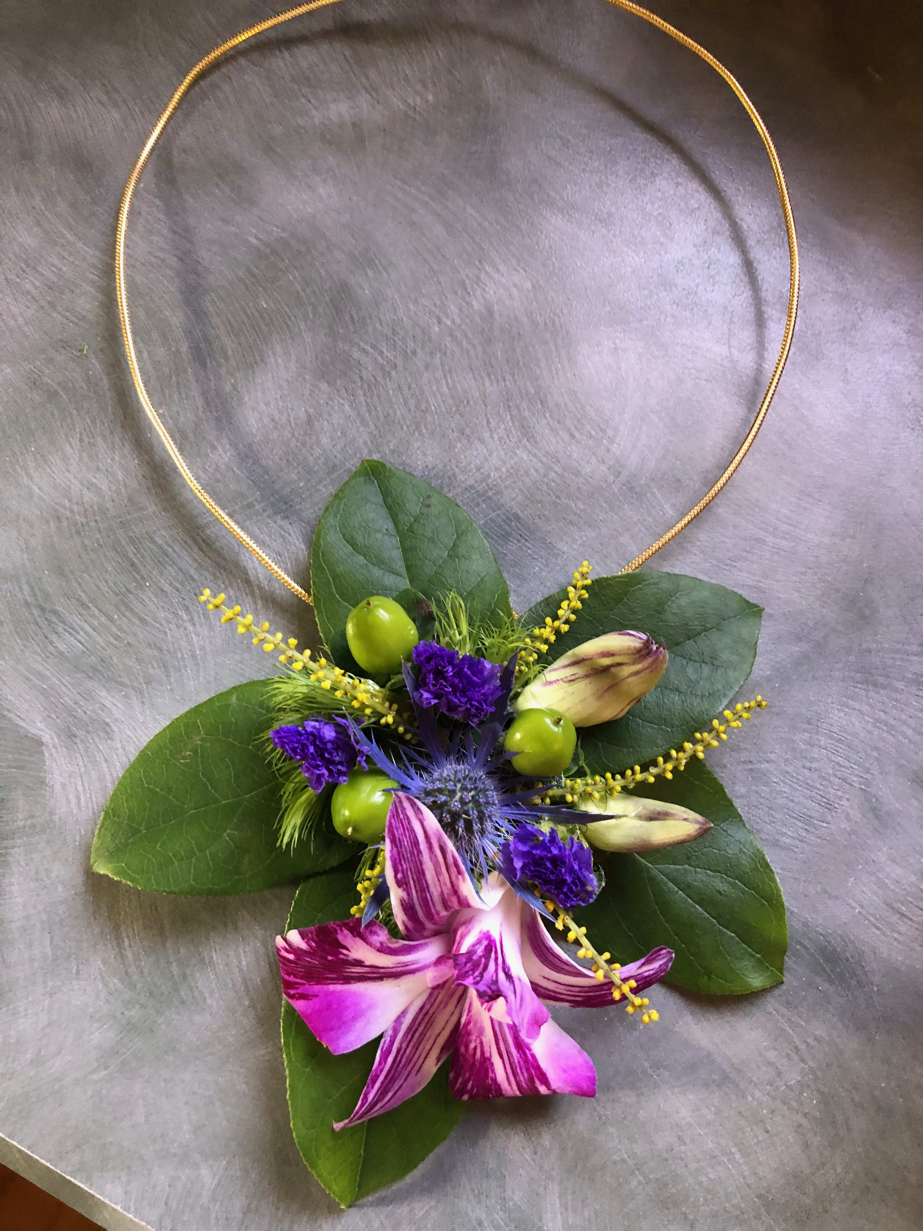 Floral necklace with purple orchid blooms and green leaves on a gold hoop