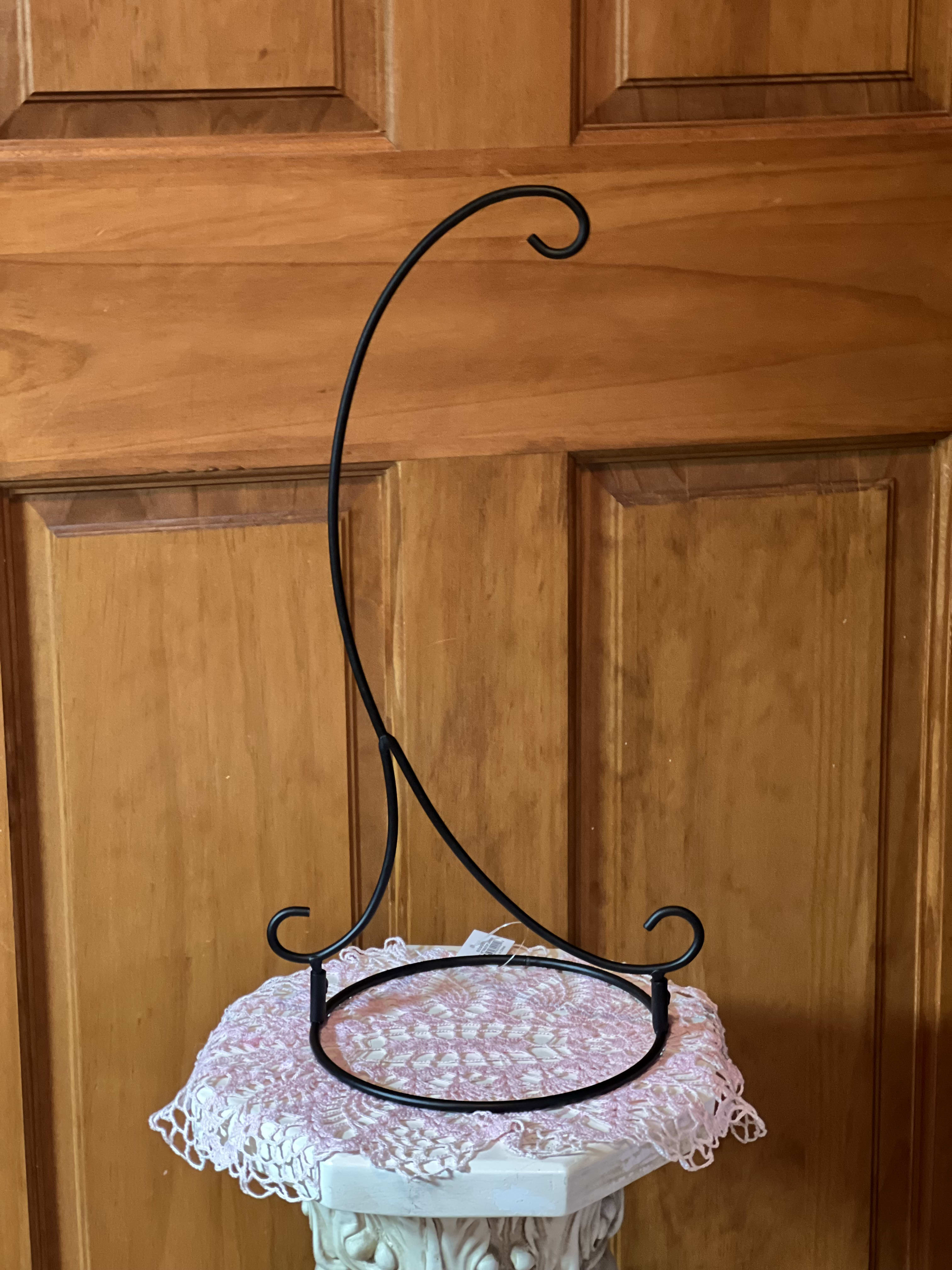 Black metal hanging stand with curled hooks on a pedestal