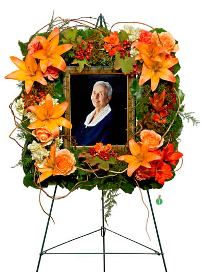 Standing floral tribute with orange lilies and roses around a framed portrait