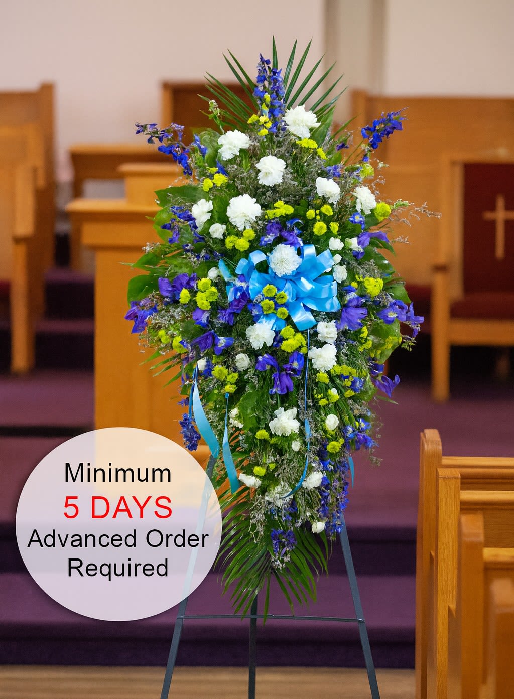 Tall blue, white, and yellow standing spray with bow on an easel in a church setting