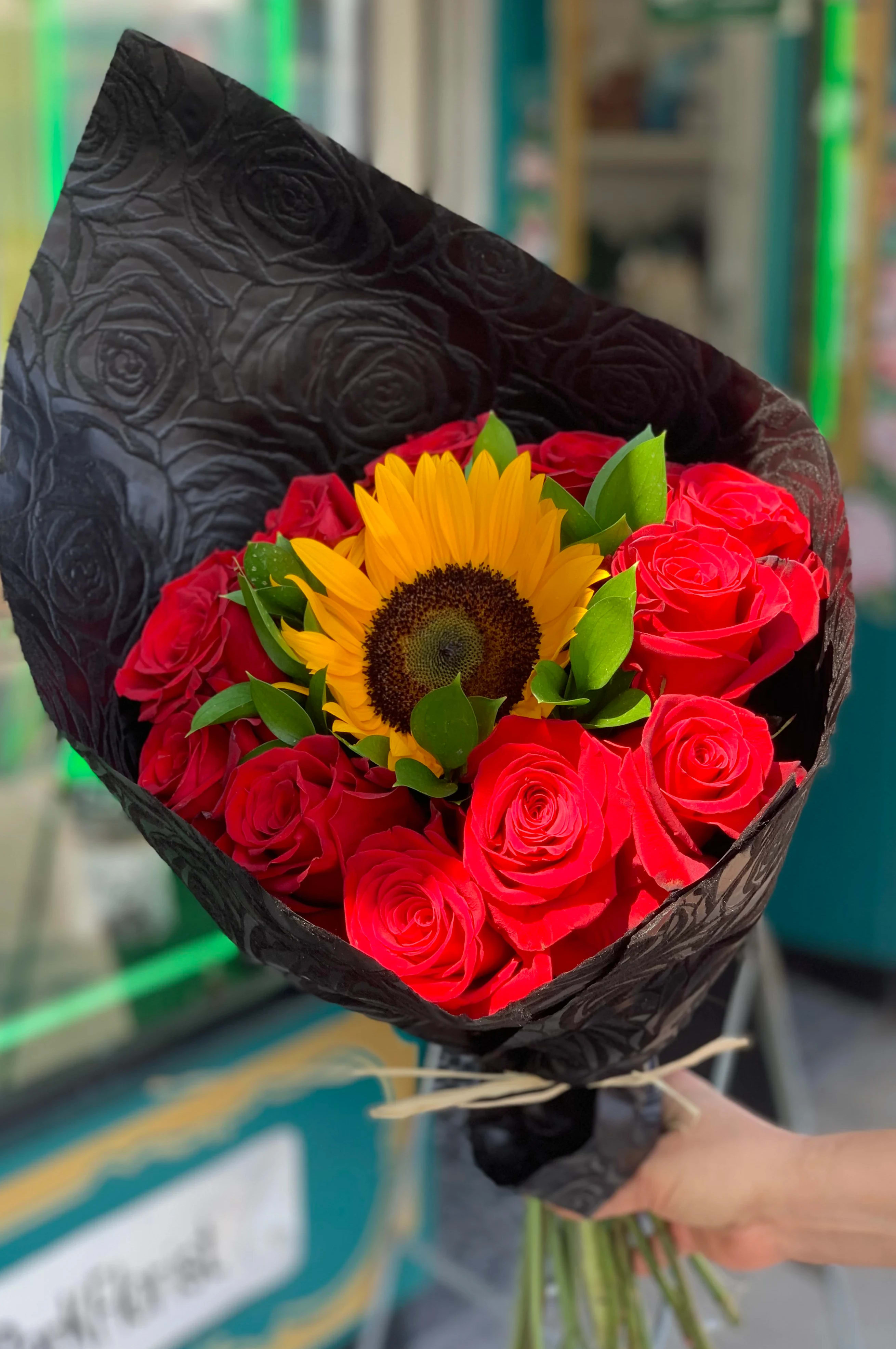Bouquet of red roses with a yellow sunflower wrapped in black paper