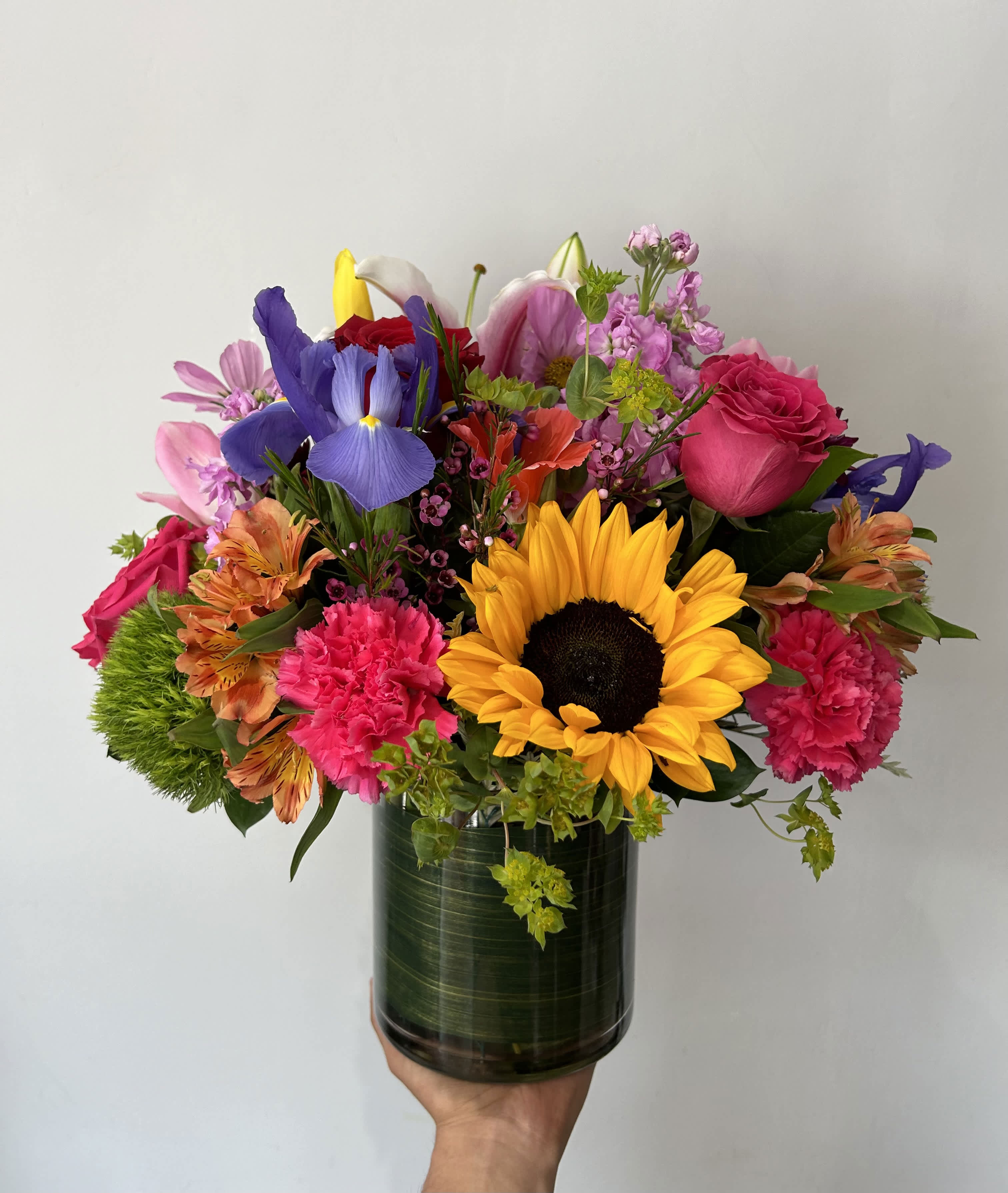 Mixed bouquet with a sunflower, roses, iris, and pink carnations in a glass vase