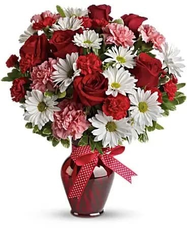 Red roses and white daisies in a red vase with a polka-dot ribbon
