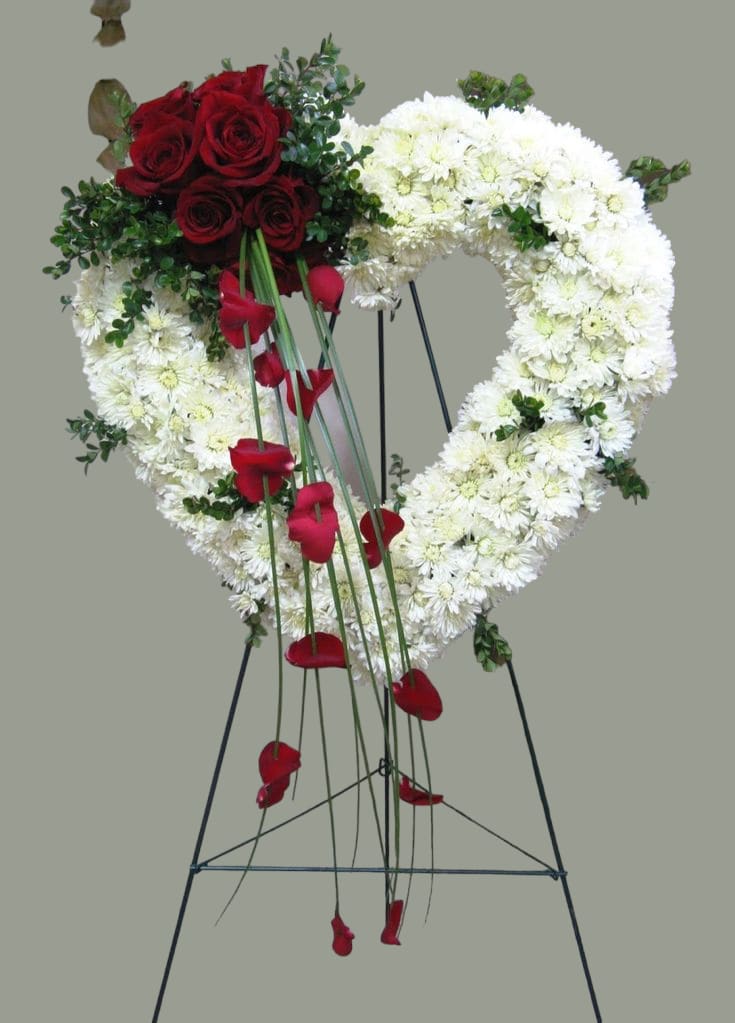 Heart-shaped floral wreath with red roses and white flowers on a stand