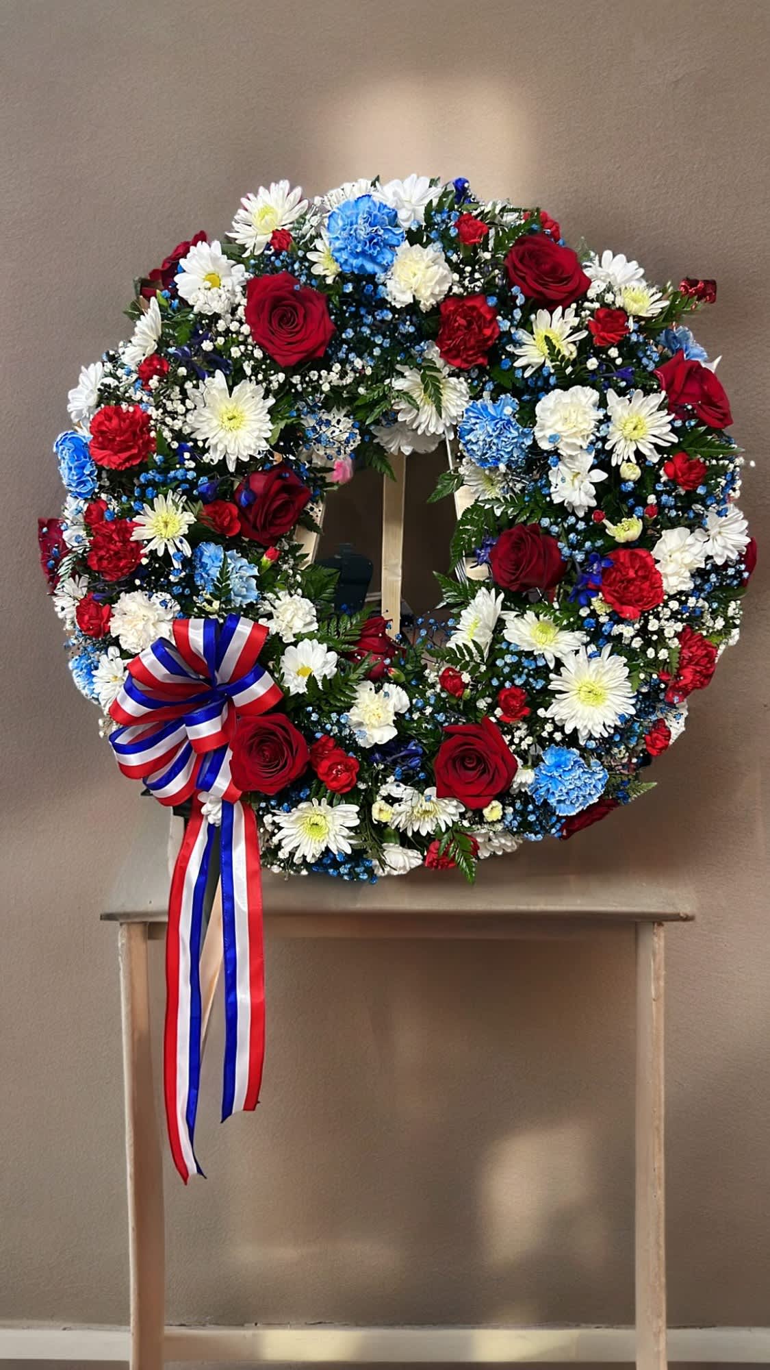Circular wreath of red, white, and blue flowers with a ribbon bow