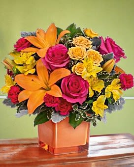 Bright bouquet of orange lilies, pink roses, and yellow flowers in a square vase