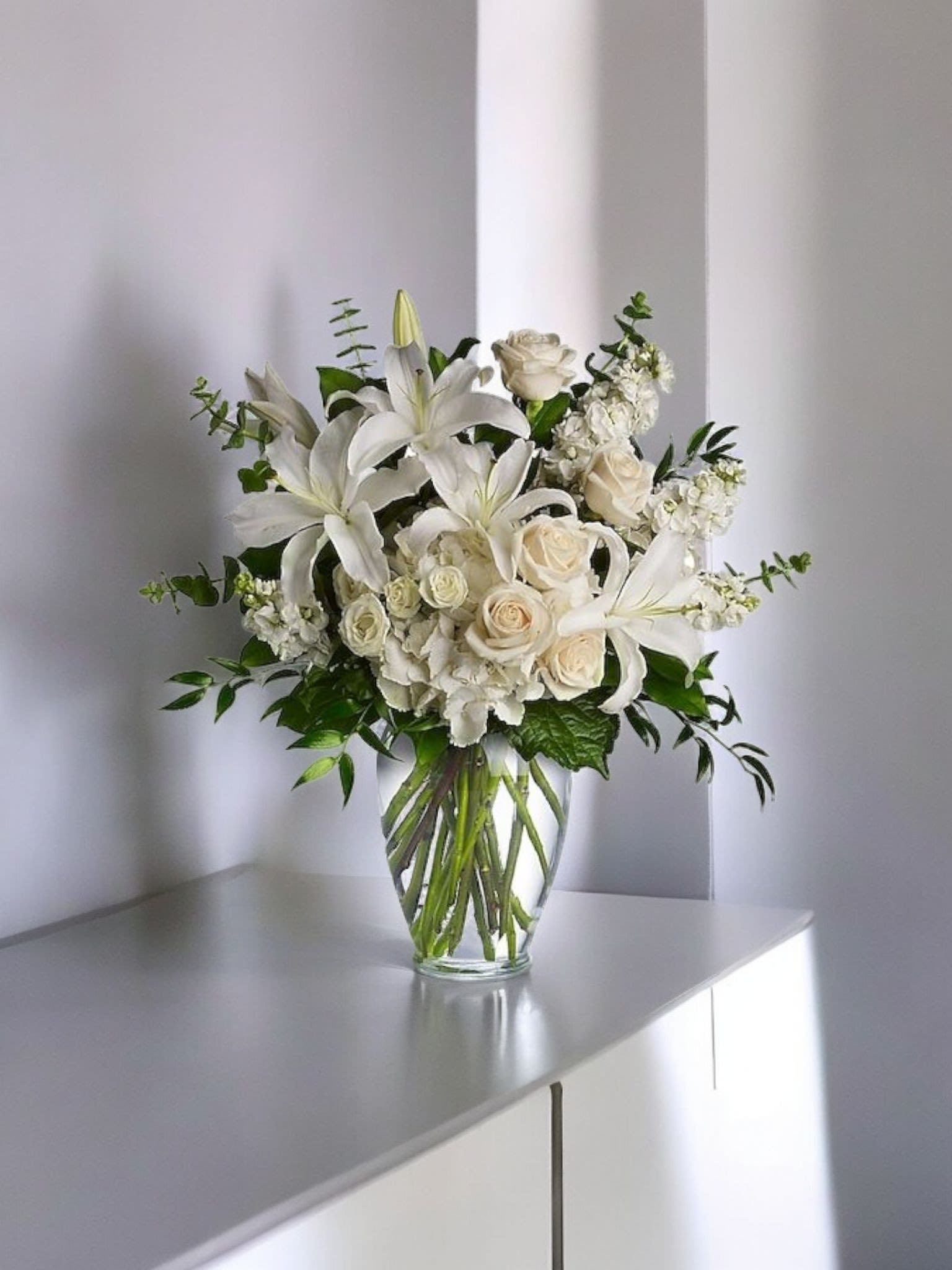 White lilies and cream roses arranged in a clear glass vase