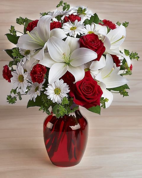 Bouquet of red roses, white lilies, and daisies in a red glass vase