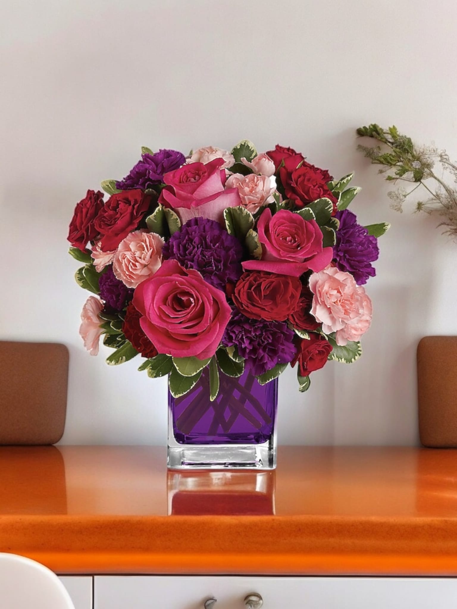Pink, red, and purple flowers arranged in a square glass vase
