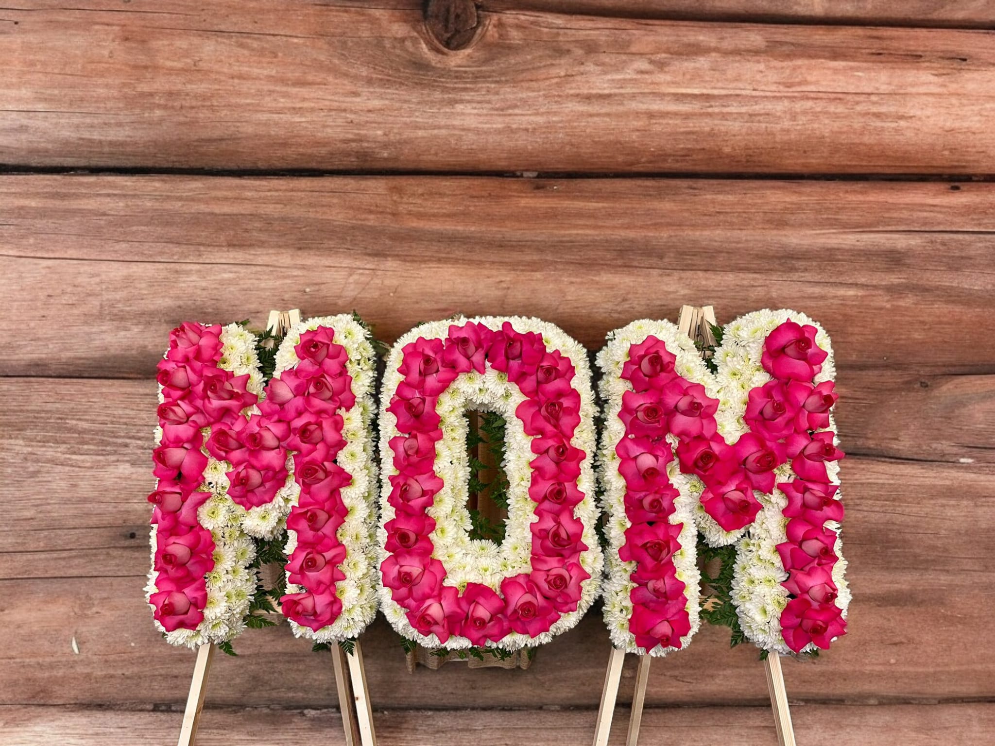 Floral standing tribute spelling MOM in pink and white flowers