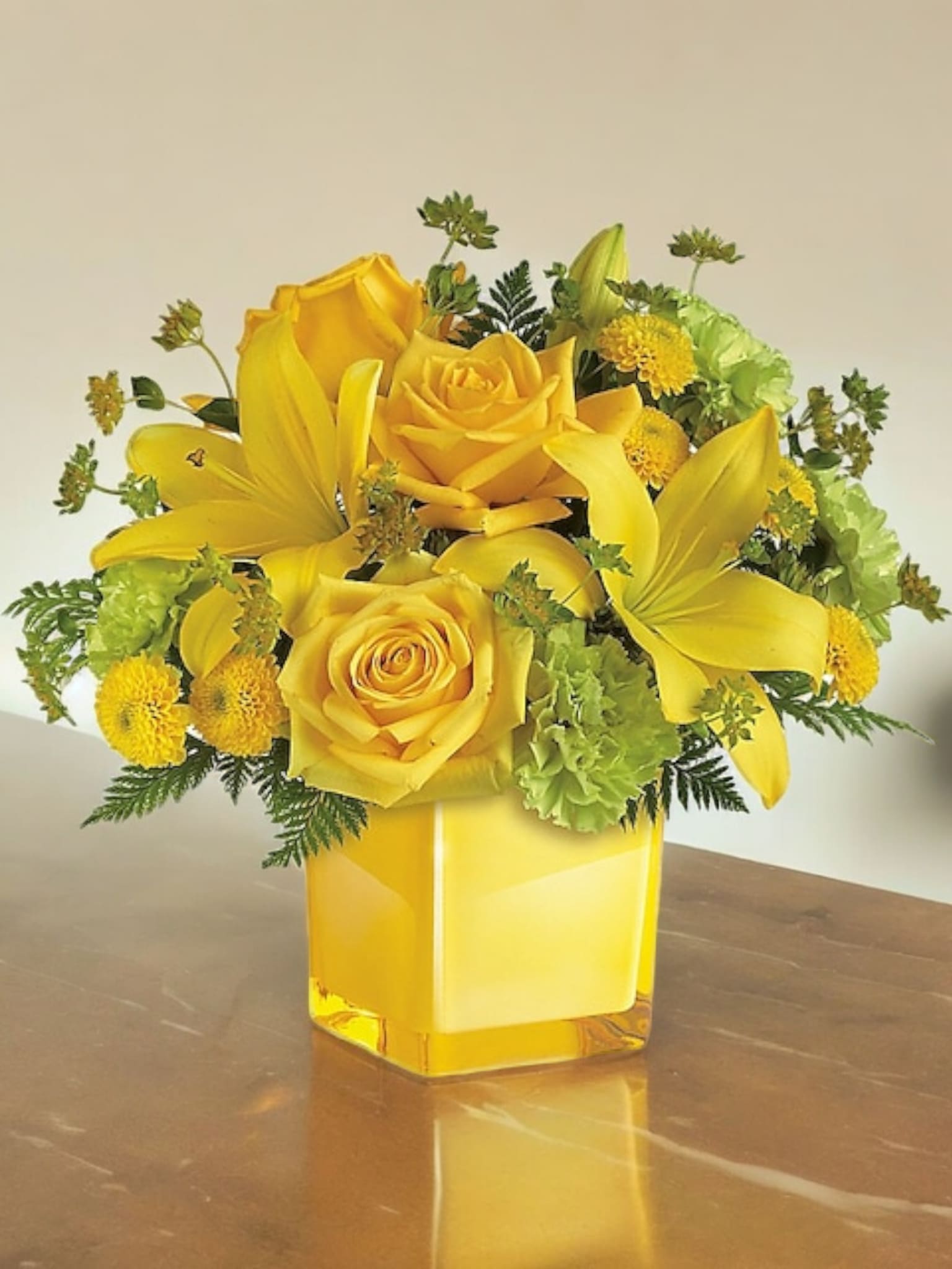 Yellow roses and lilies arranged in a square glass vase