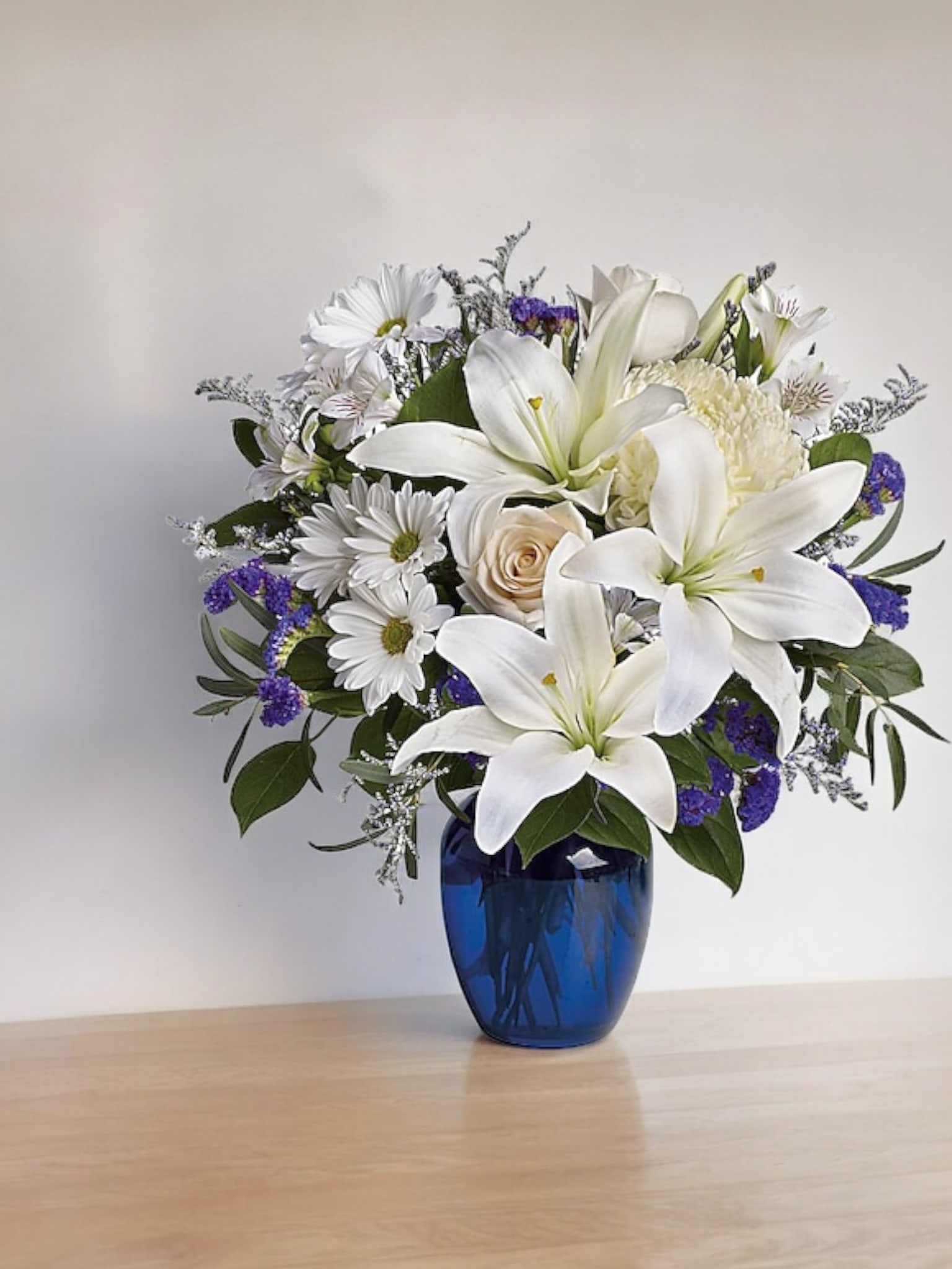White lilies and daisies arranged in a blue vase