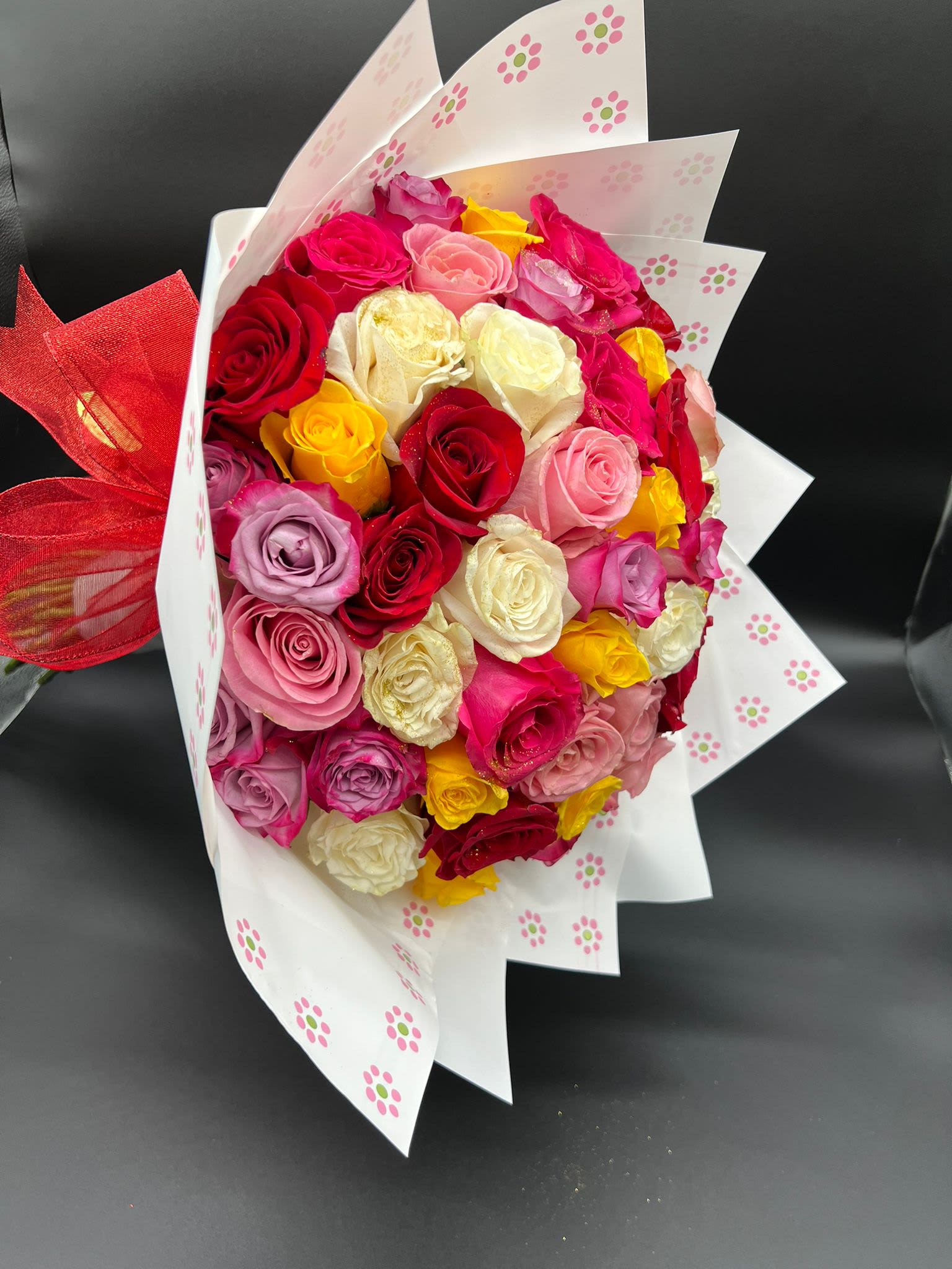 Bouquet of multicolored roses wrapped in white paper with a red ribbon