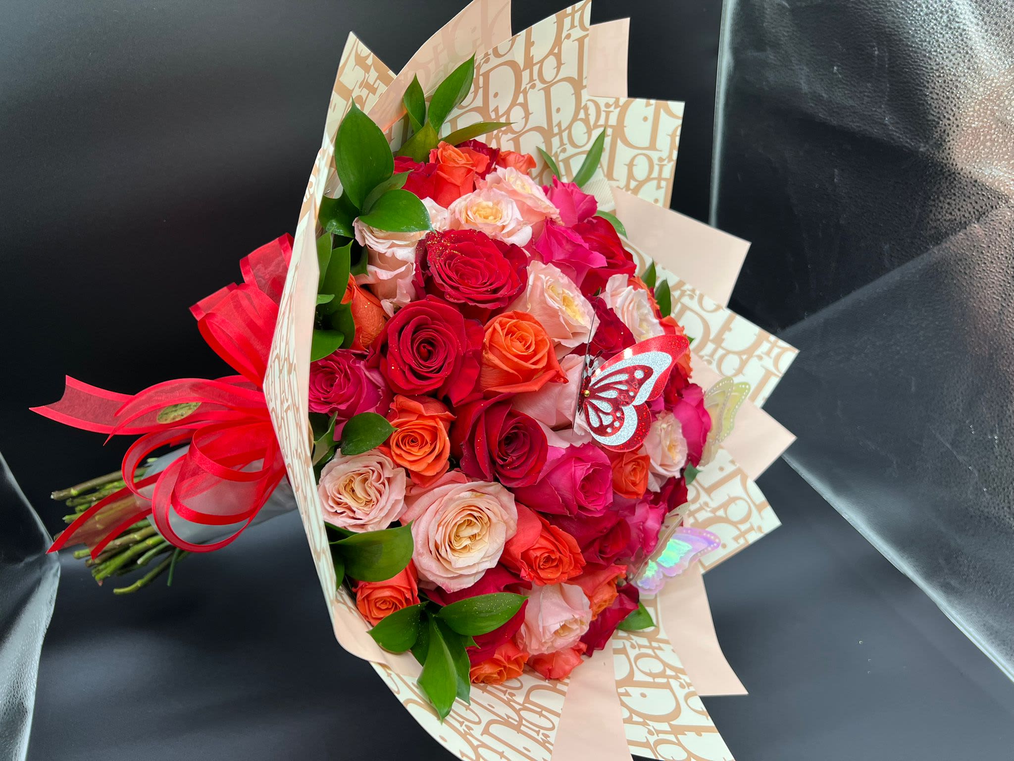 Bouquet of red, pink, and peach roses wrapped in patterned paper