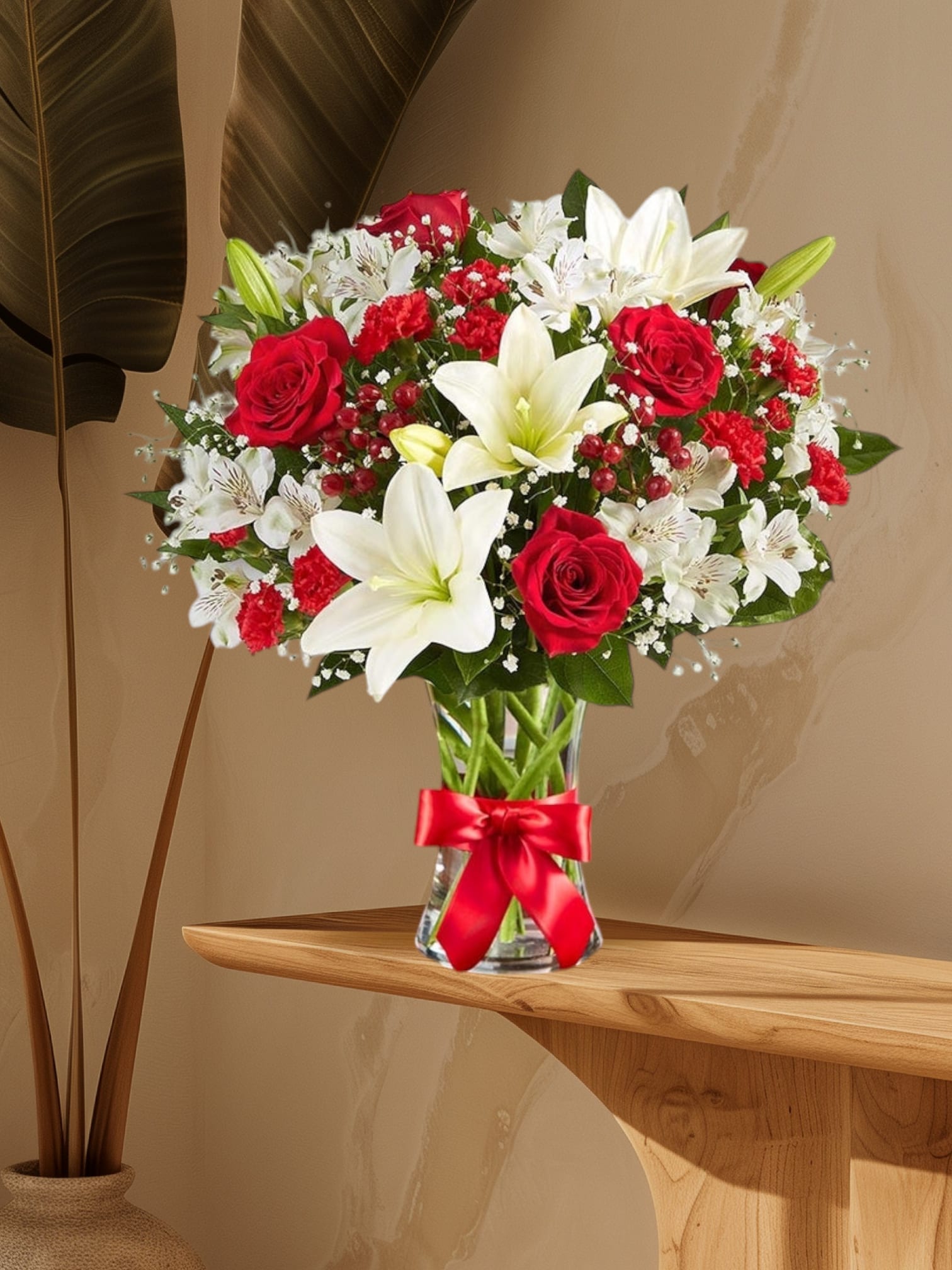 Red roses and white lilies arranged in a clear glass vase with a red ribbon