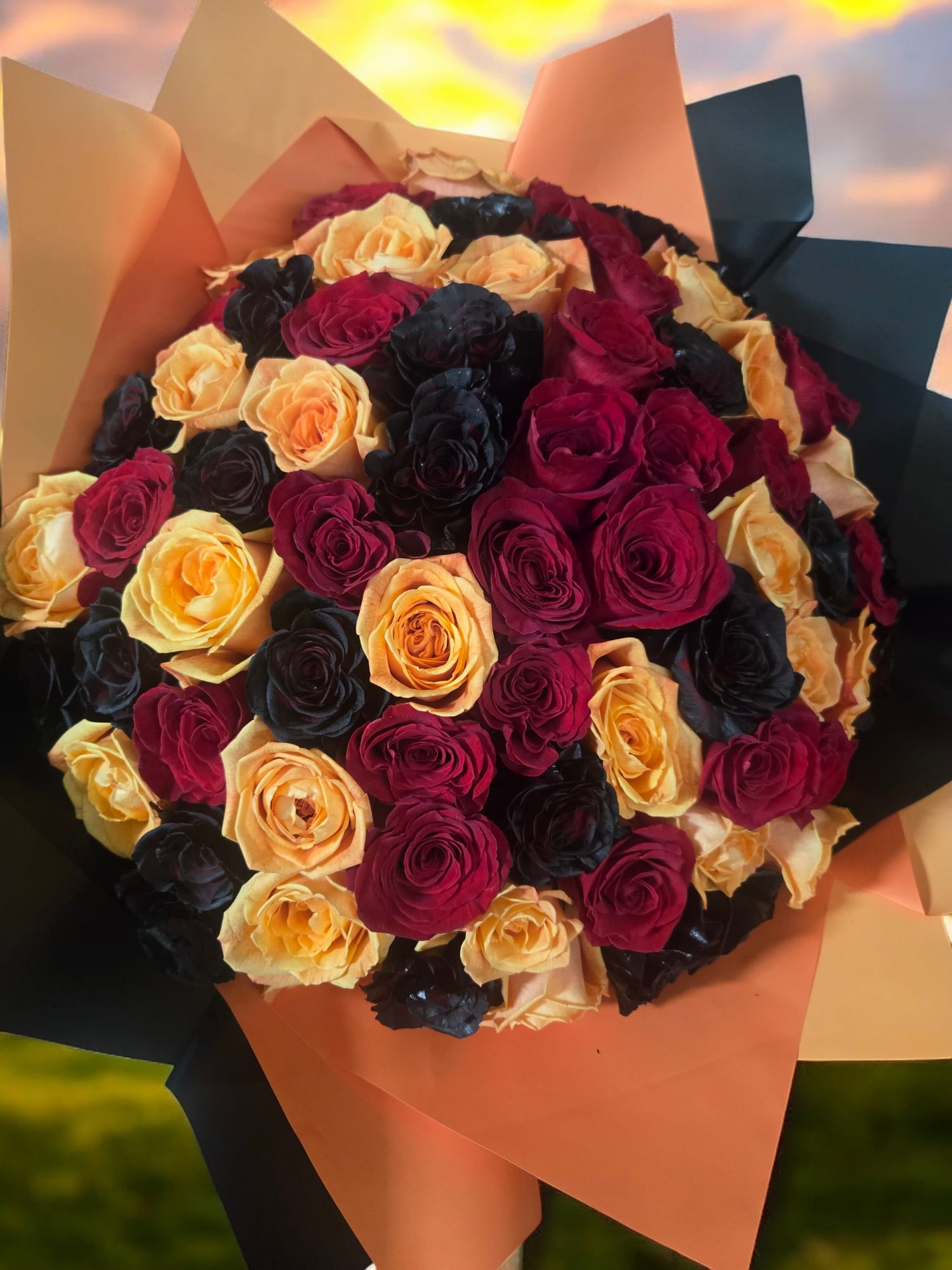 Bouquet of red, peach, and black roses wrapped in peach and black paper
